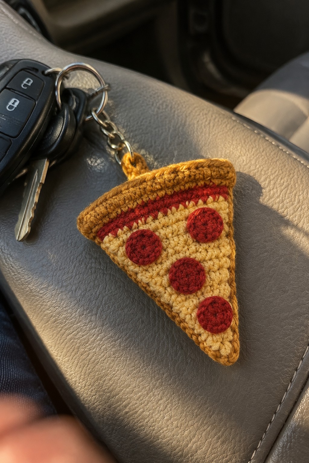 Crocheted pizza slice keychain with pepperoni on black car key atop gray seat
