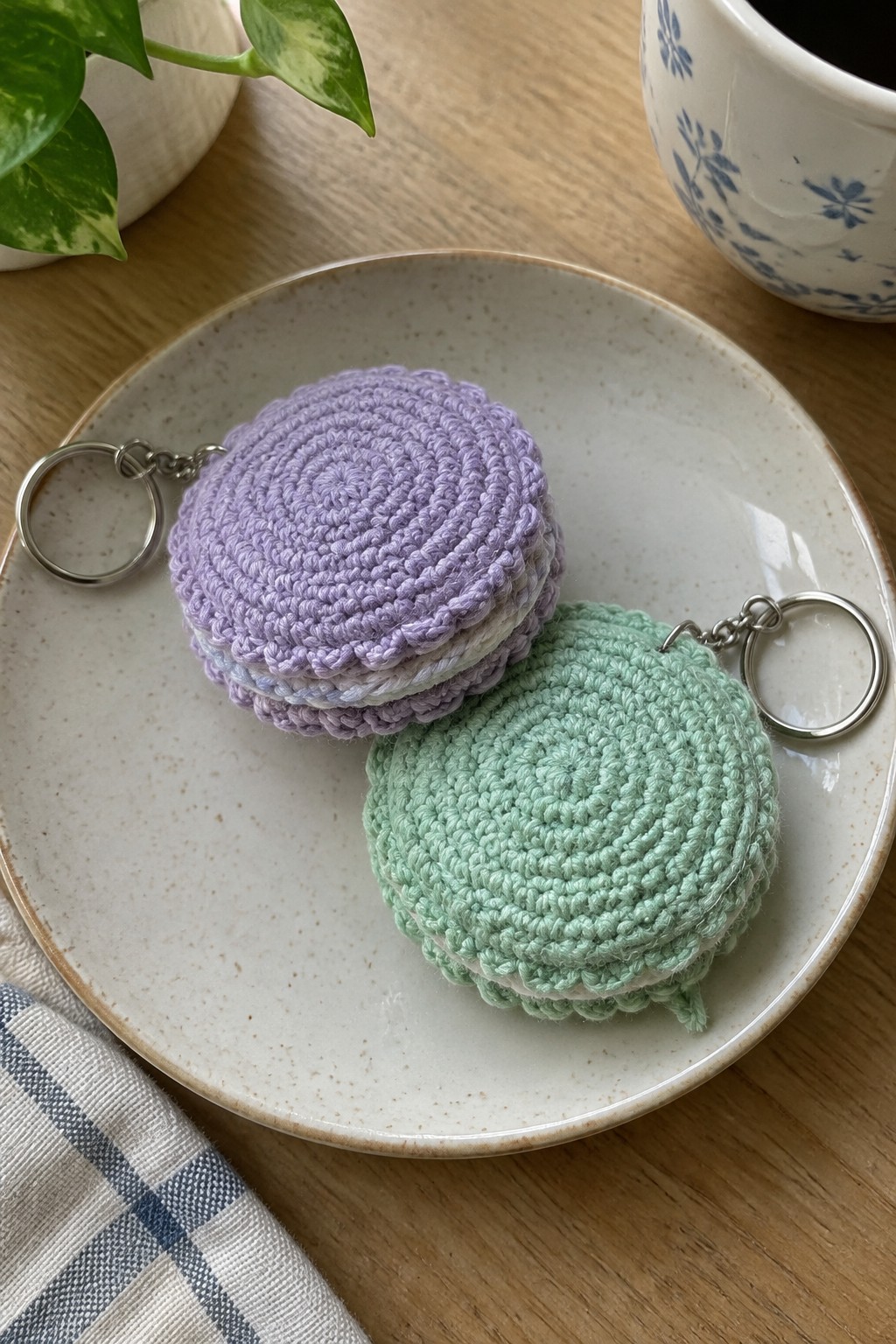 Two crocheted macaron keychains, lavender and mint, on a speckled plate.