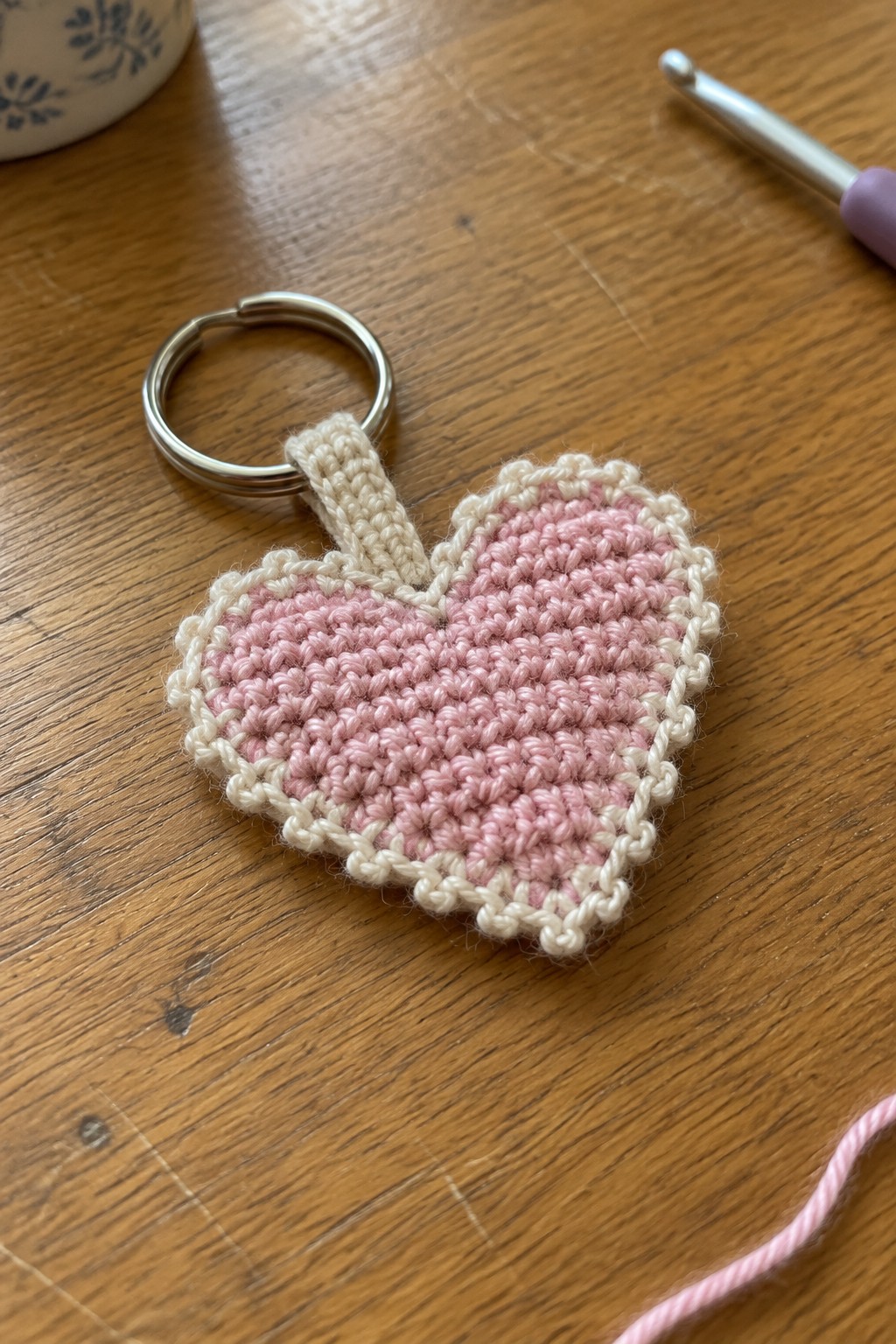 Pink crocheted heart keychain with white border on silver ring atop wooden table