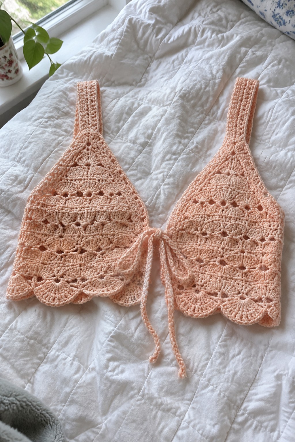 Two peach crocheted halter tops with ties on a white quilted bed