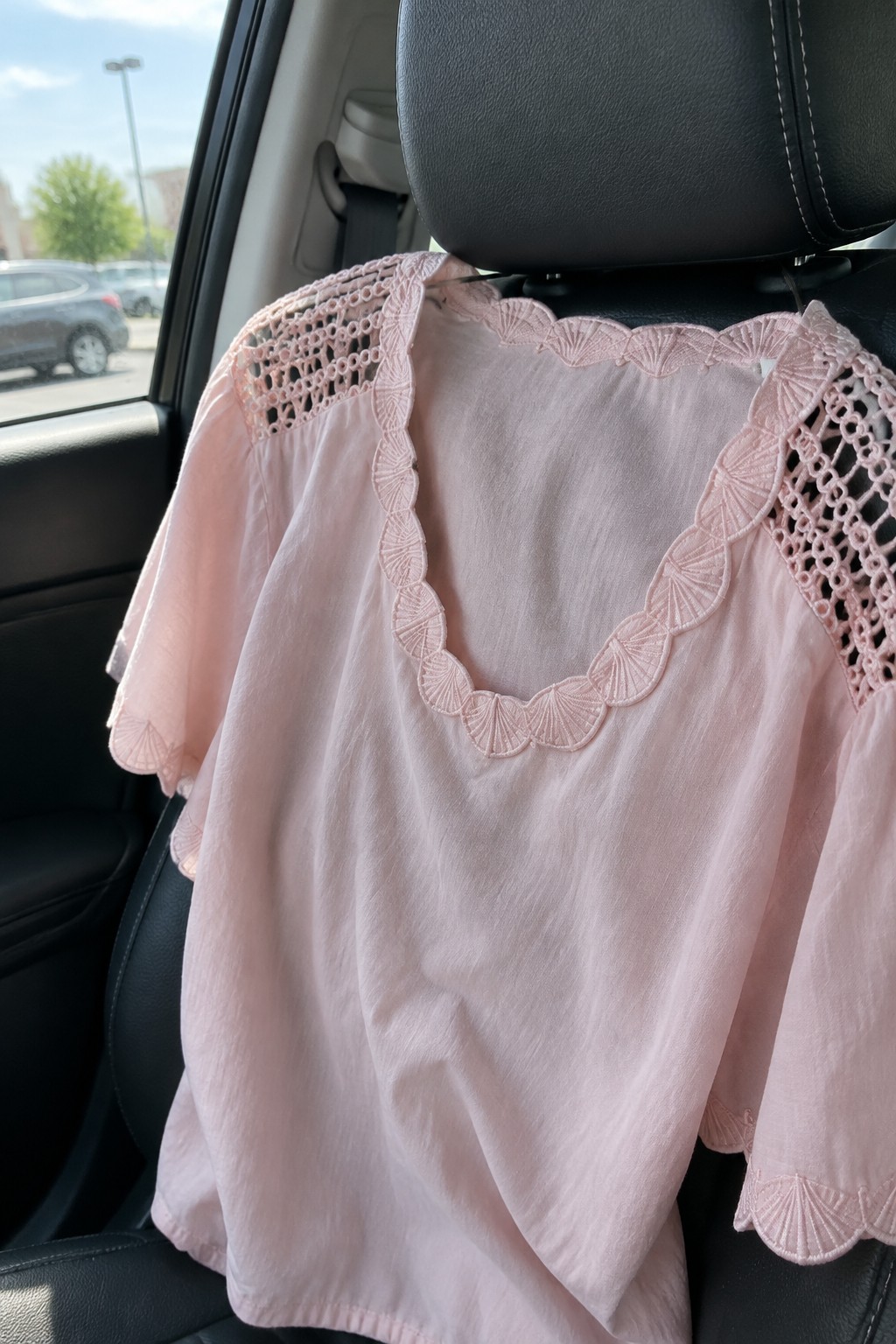 Light pink blouse with pink crochet lace trim on the neckline and sleeves resting on a car seat.