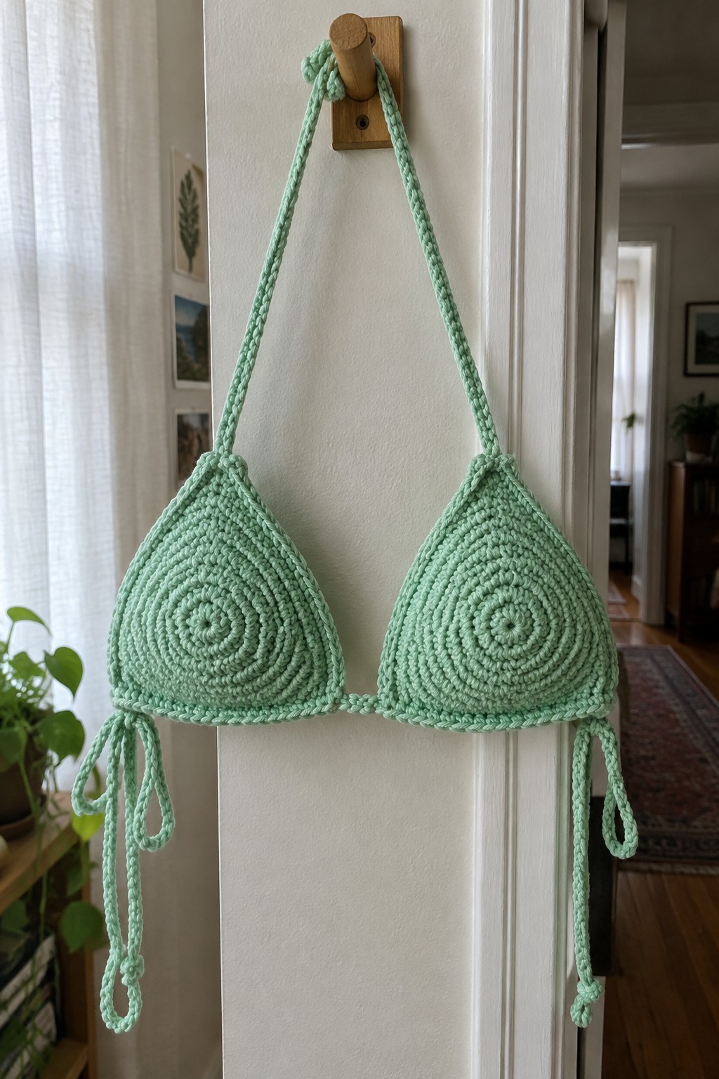 Mint green crocheted bikini top hanging from wooden hook on white door