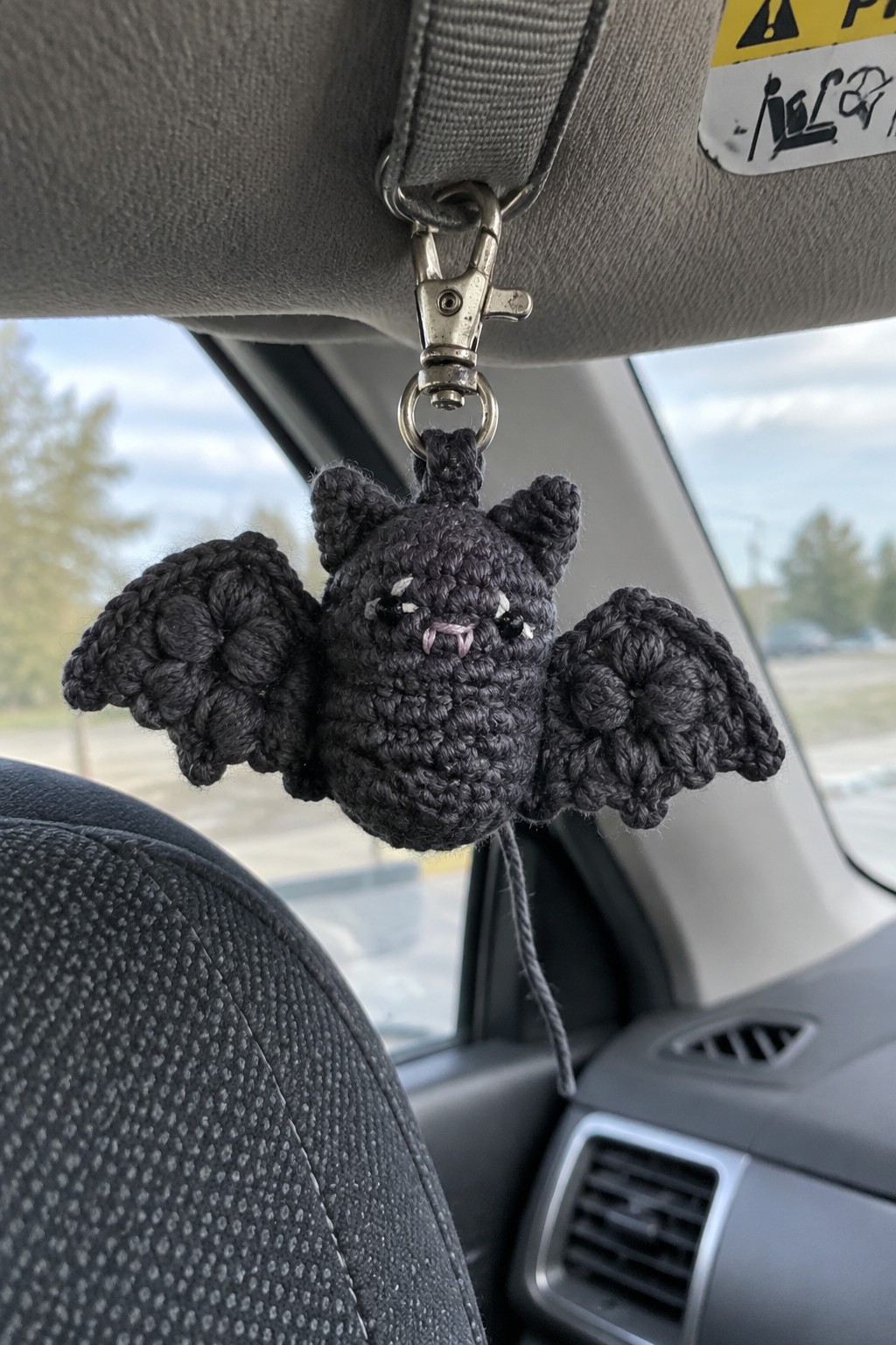 Black crocheted bat keychain dangling from car ceiling hook, wings spread wide