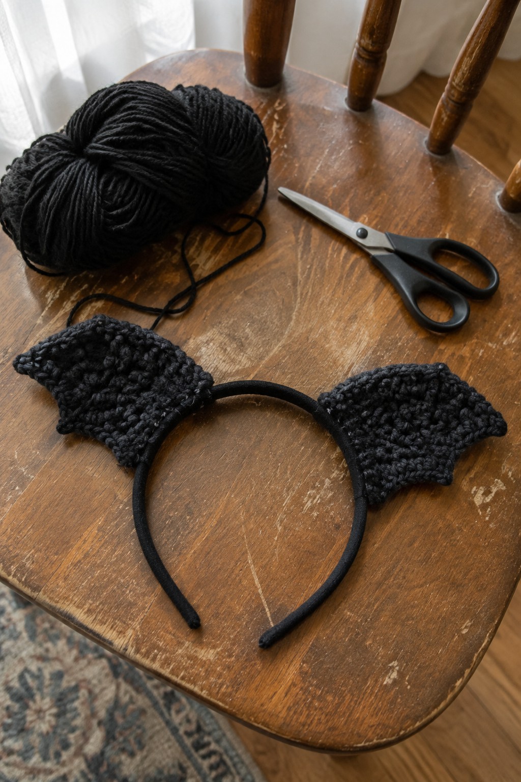 Black crocheted bat wings on headband with yarn and scissors on wooden chair