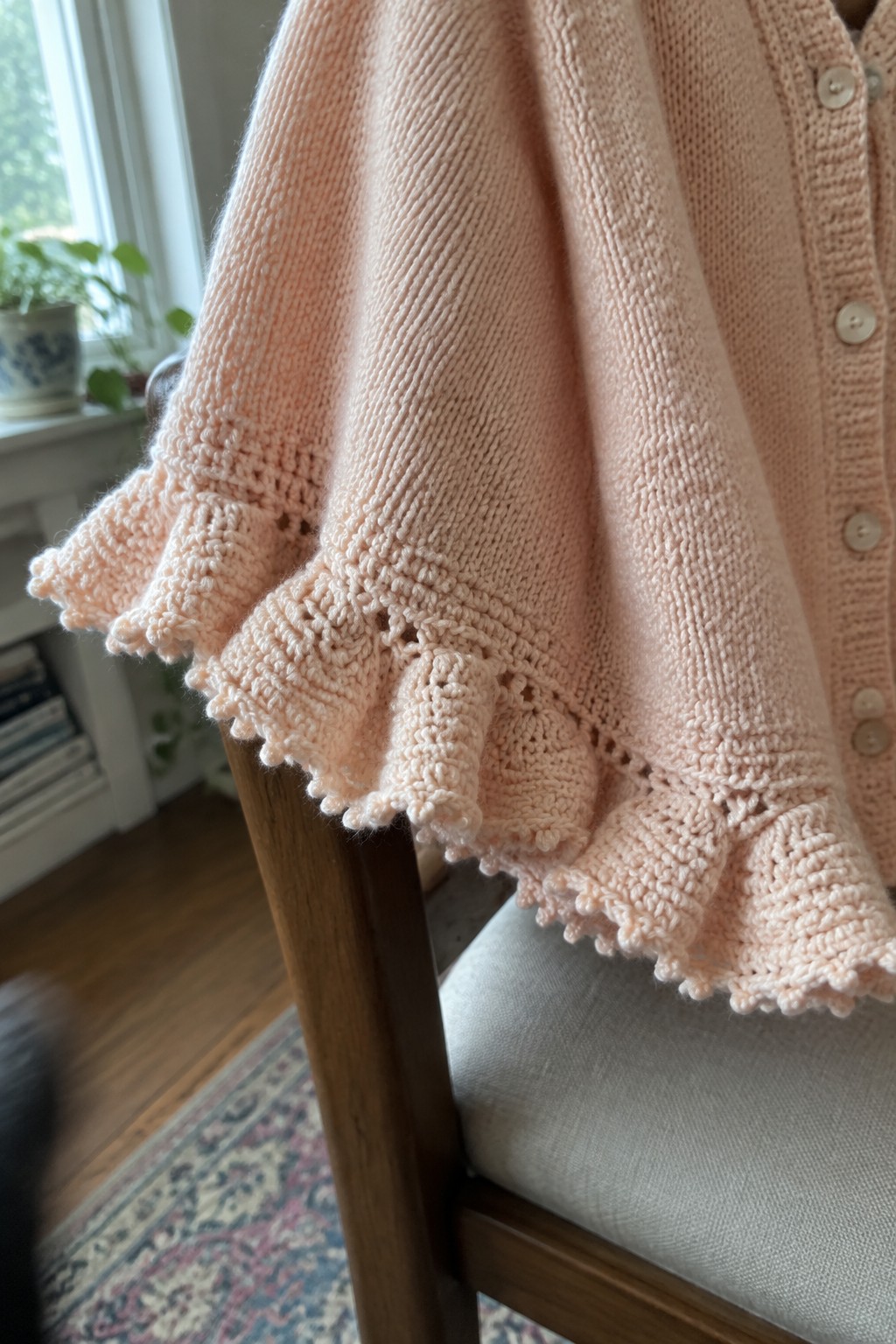Pale pink knitted cardigan with ruffled lace hem on wooden chair