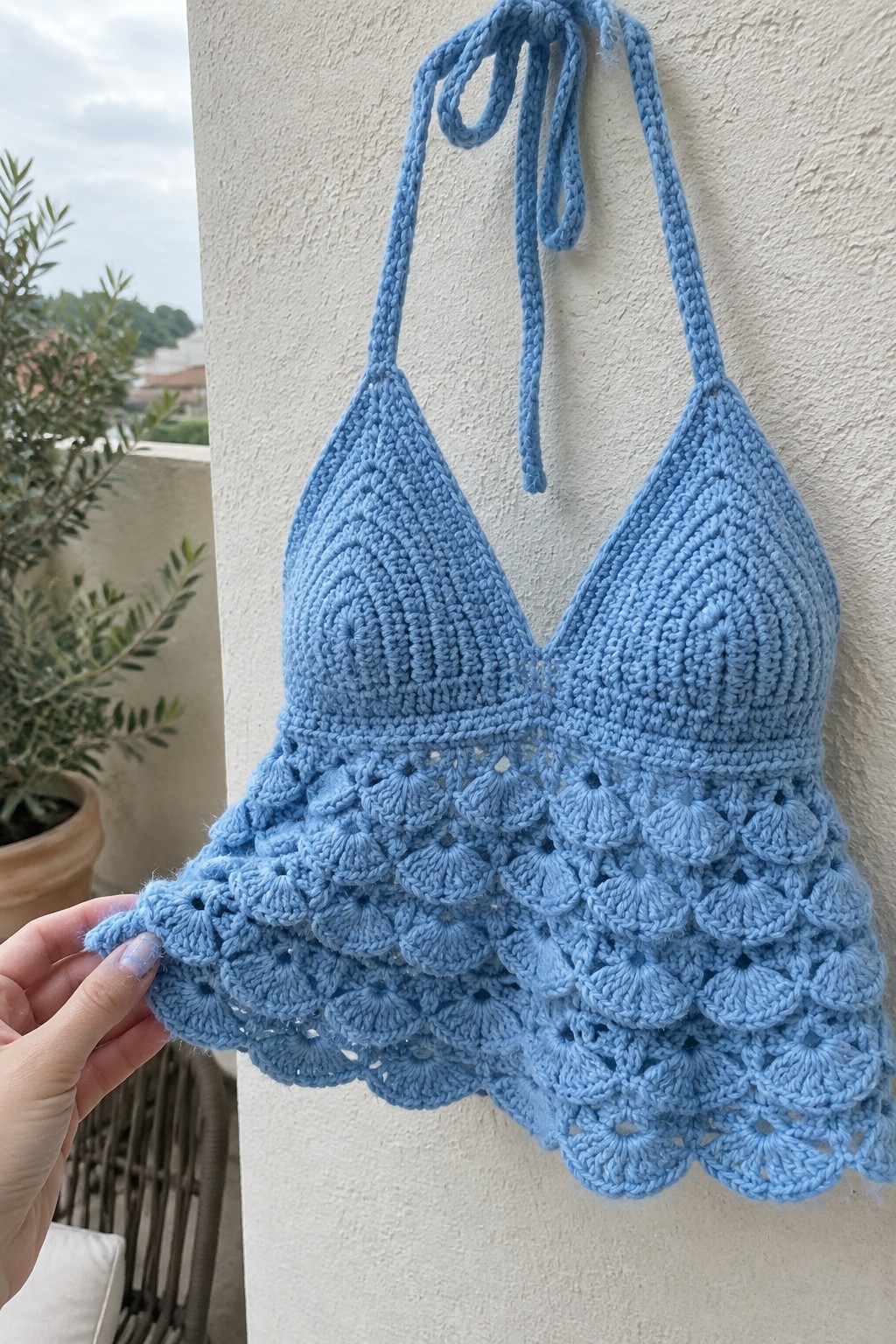 Hand holding light blue crocheted halter top with scalloped hem outdoors