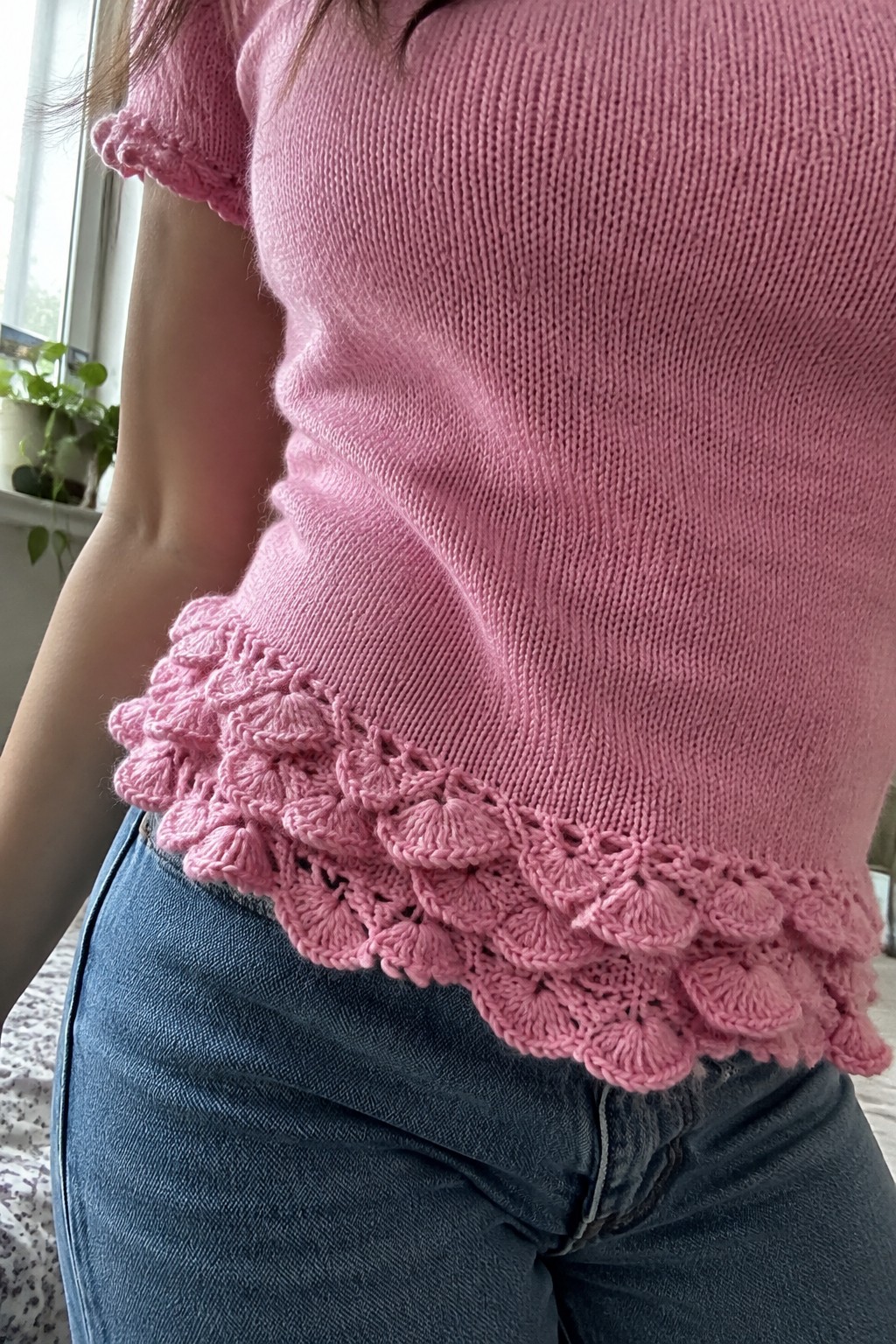 Pink knitted top with scalloped ruffle hem paired with blue jeans