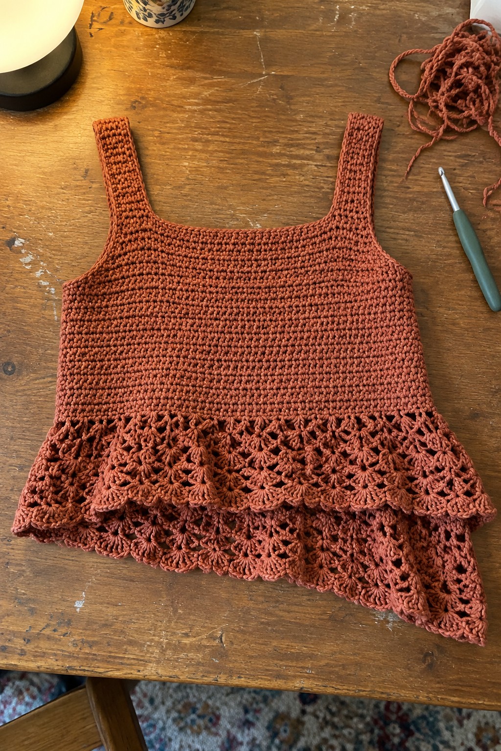 Rust crocheted tank top with lacy scalloped ruffle hem beside hook on wood