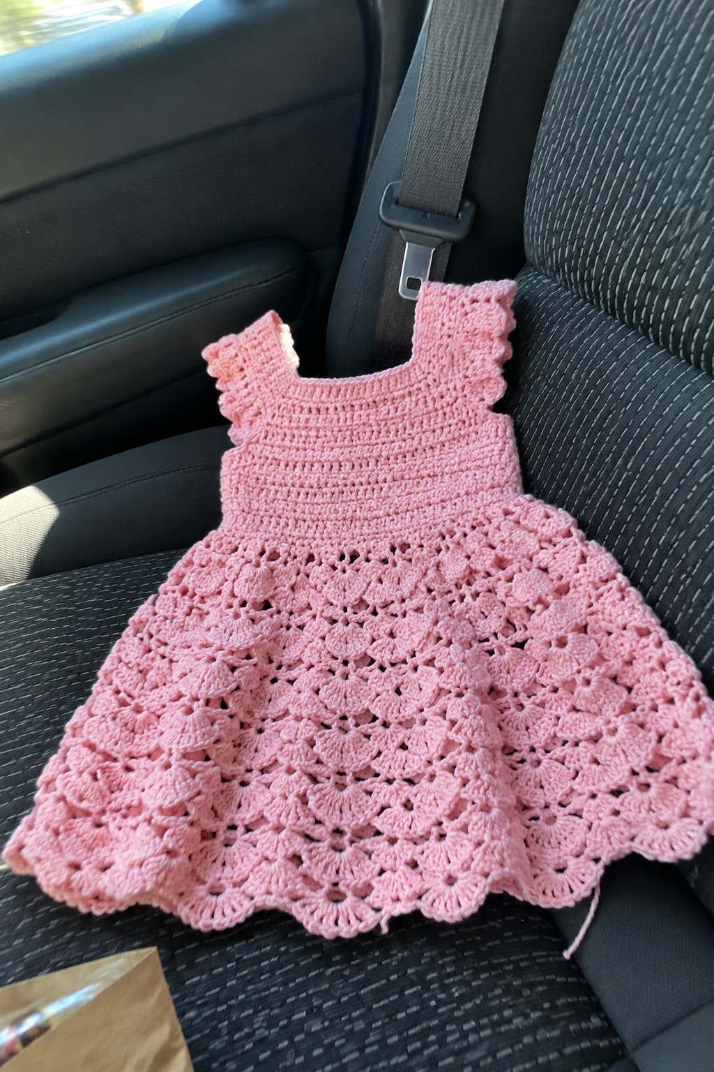 Pink crocheted dress with scalloped hem on black car seat
