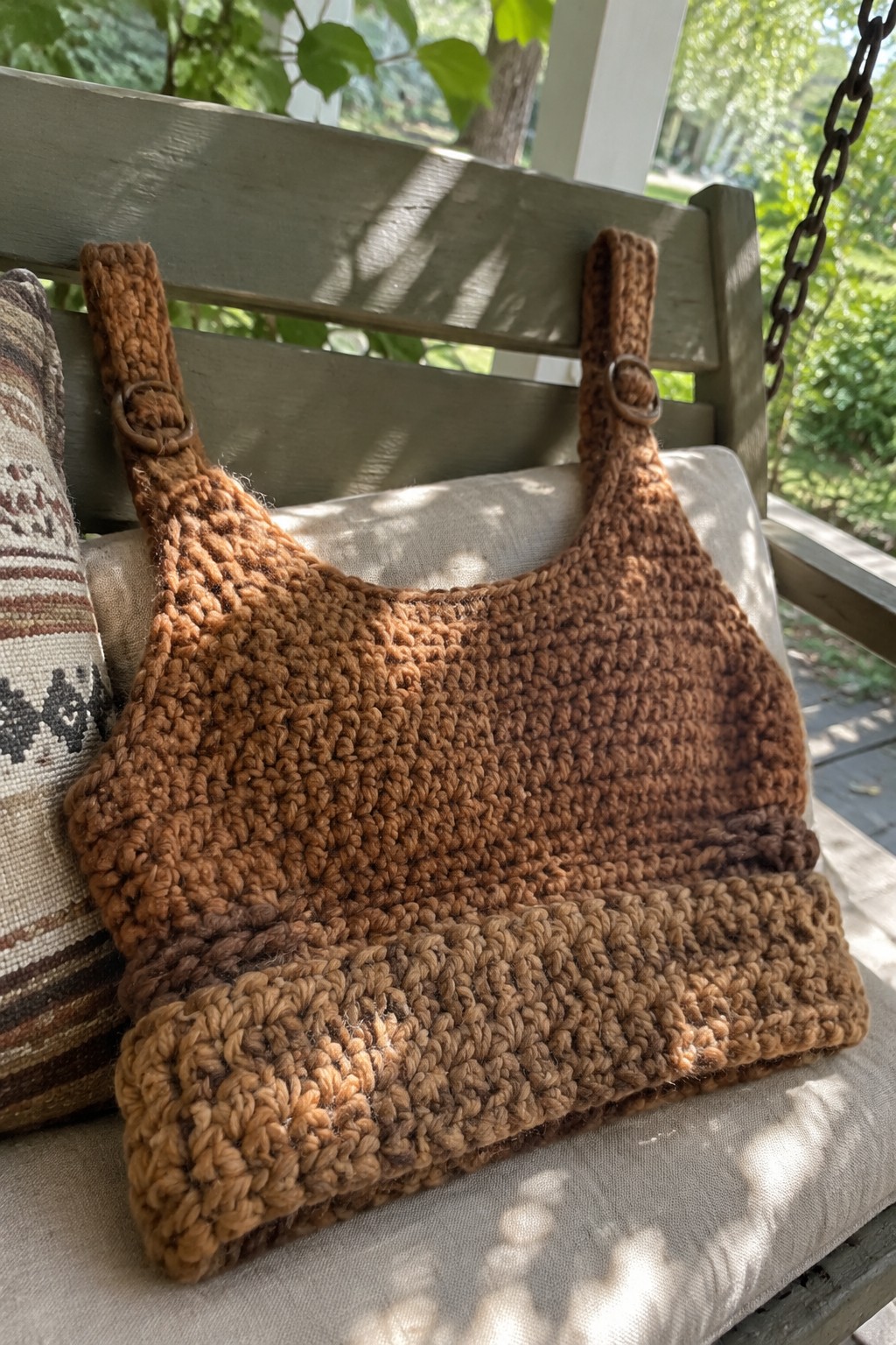 Brown crocheted crop top with buckled straps on wooden porch chair cushion.