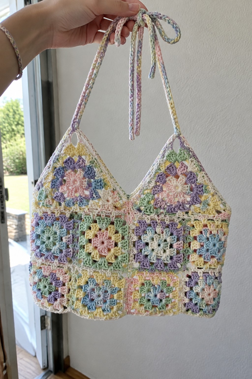 Hand holding pastel granny square crocheted bag with braided straps.