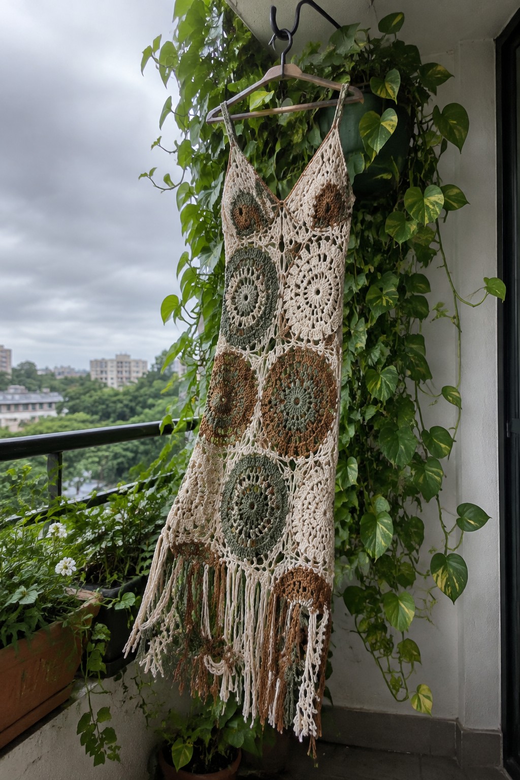 Crocheted dress with circular motifs and fringe hanging on balcony amid green plants