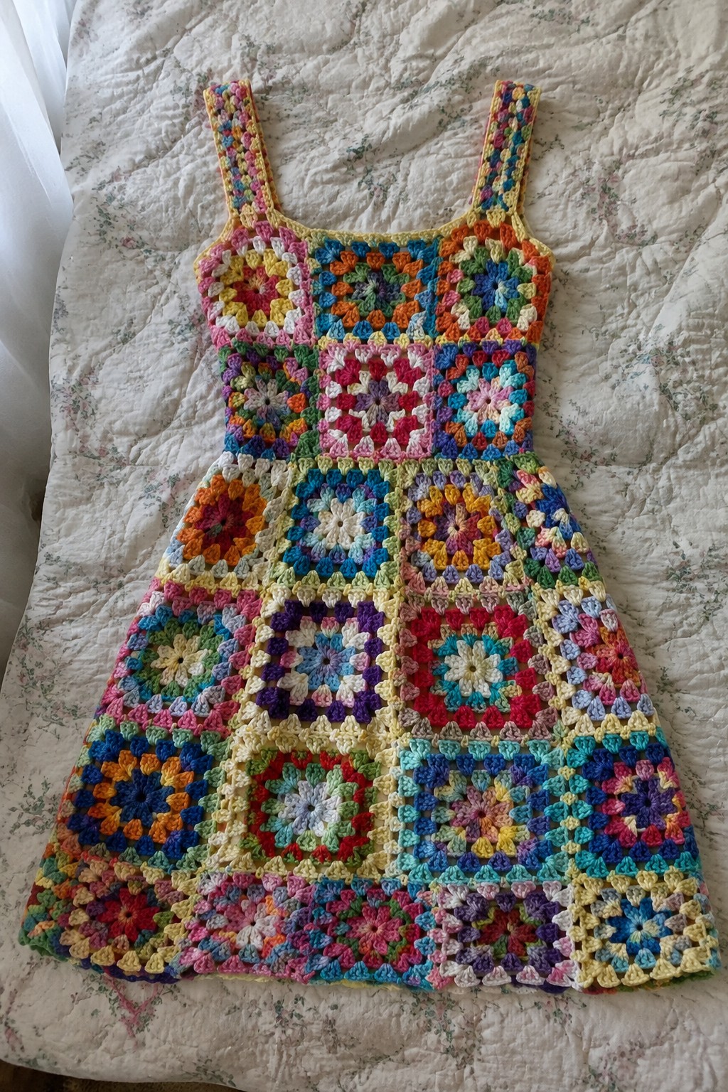 A colorful crochet dress made from granny squares laid flat on a quilted surface.