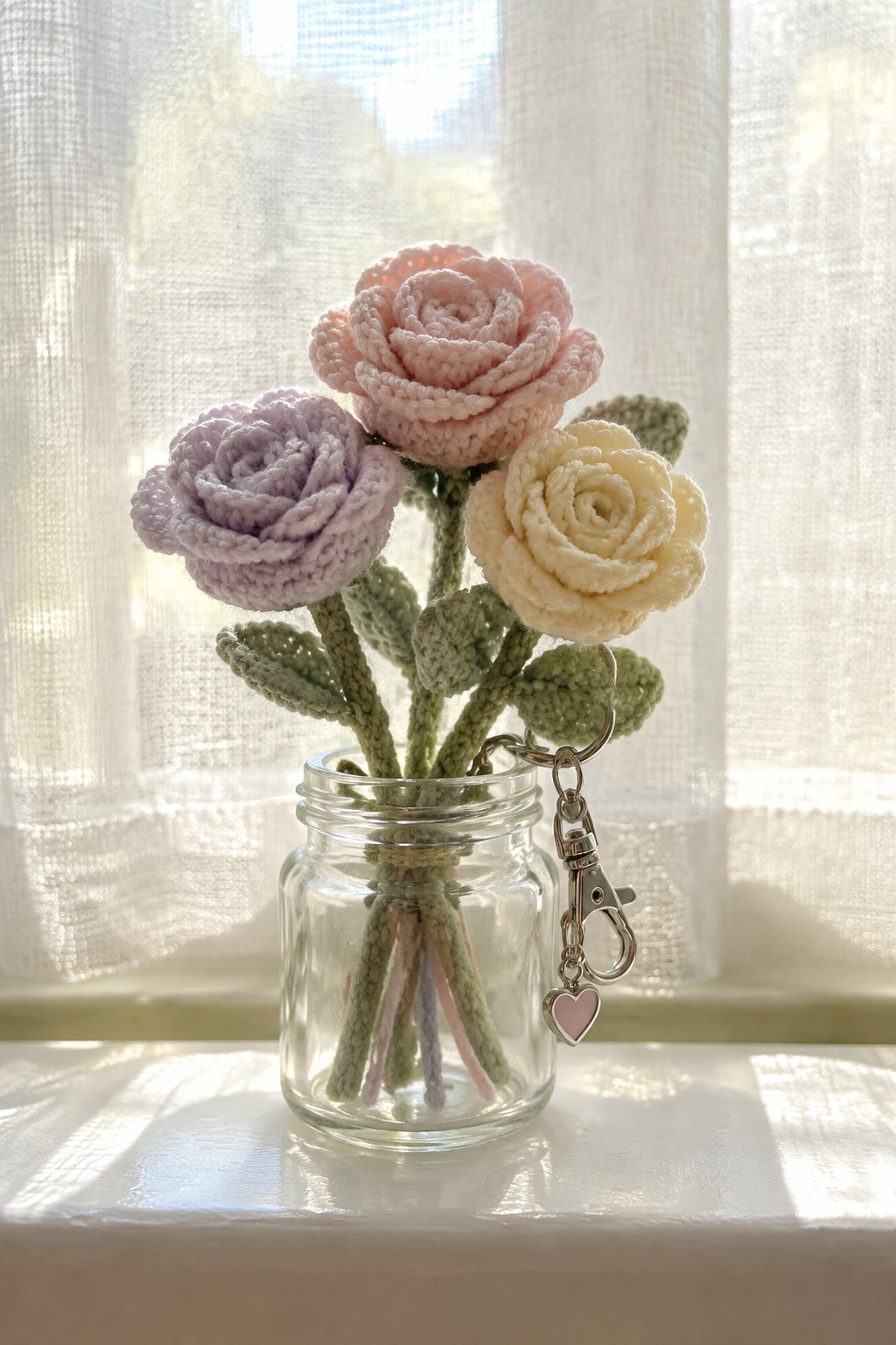 Three crocheted roses in pink, lavender, and cream inside glass jar with heart keychain