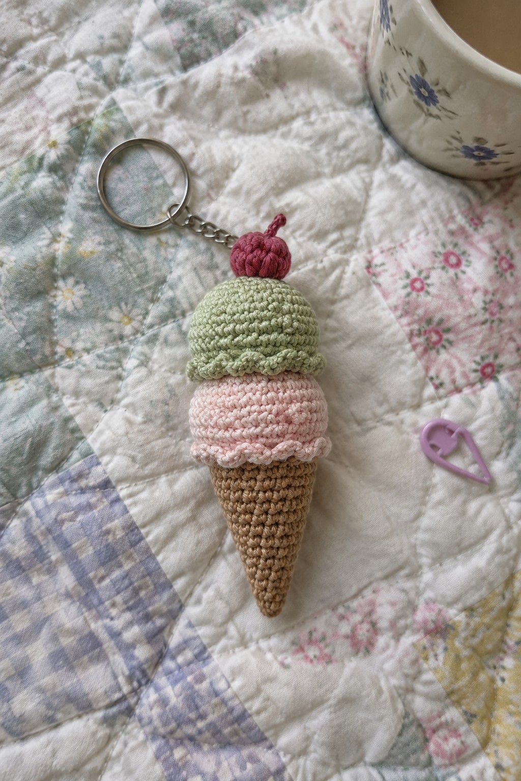 Crocheted ice cream cone keychain with pink, green scoops and cherry on floral quilt