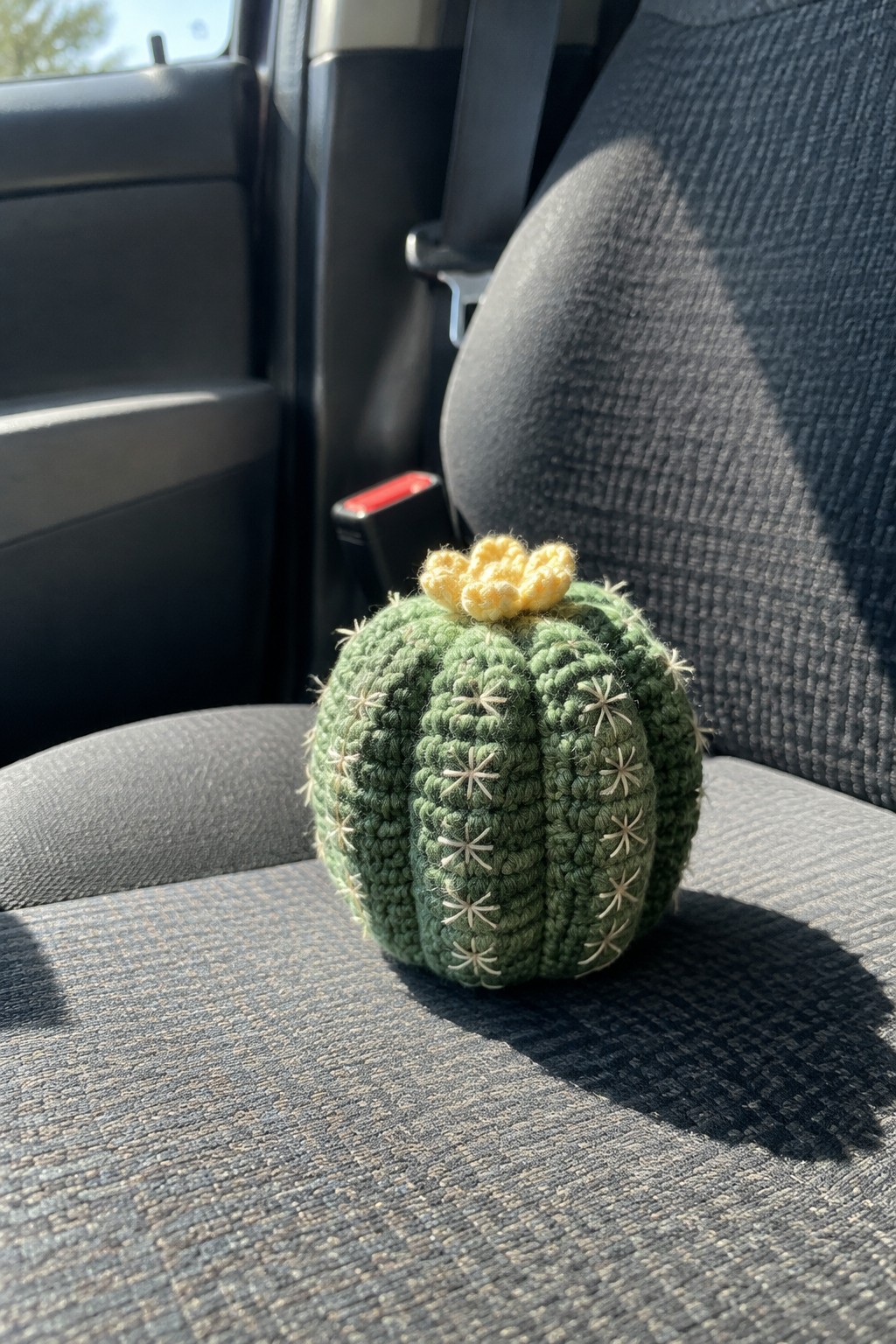 Green crocheted cactus with yellow flower on gray car seat in sunlight