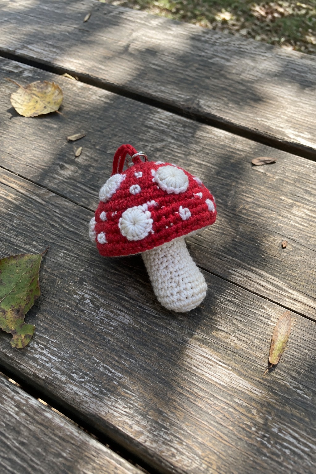 Red crocheted mushroom with white dots, white stem, and keyring on wooden table