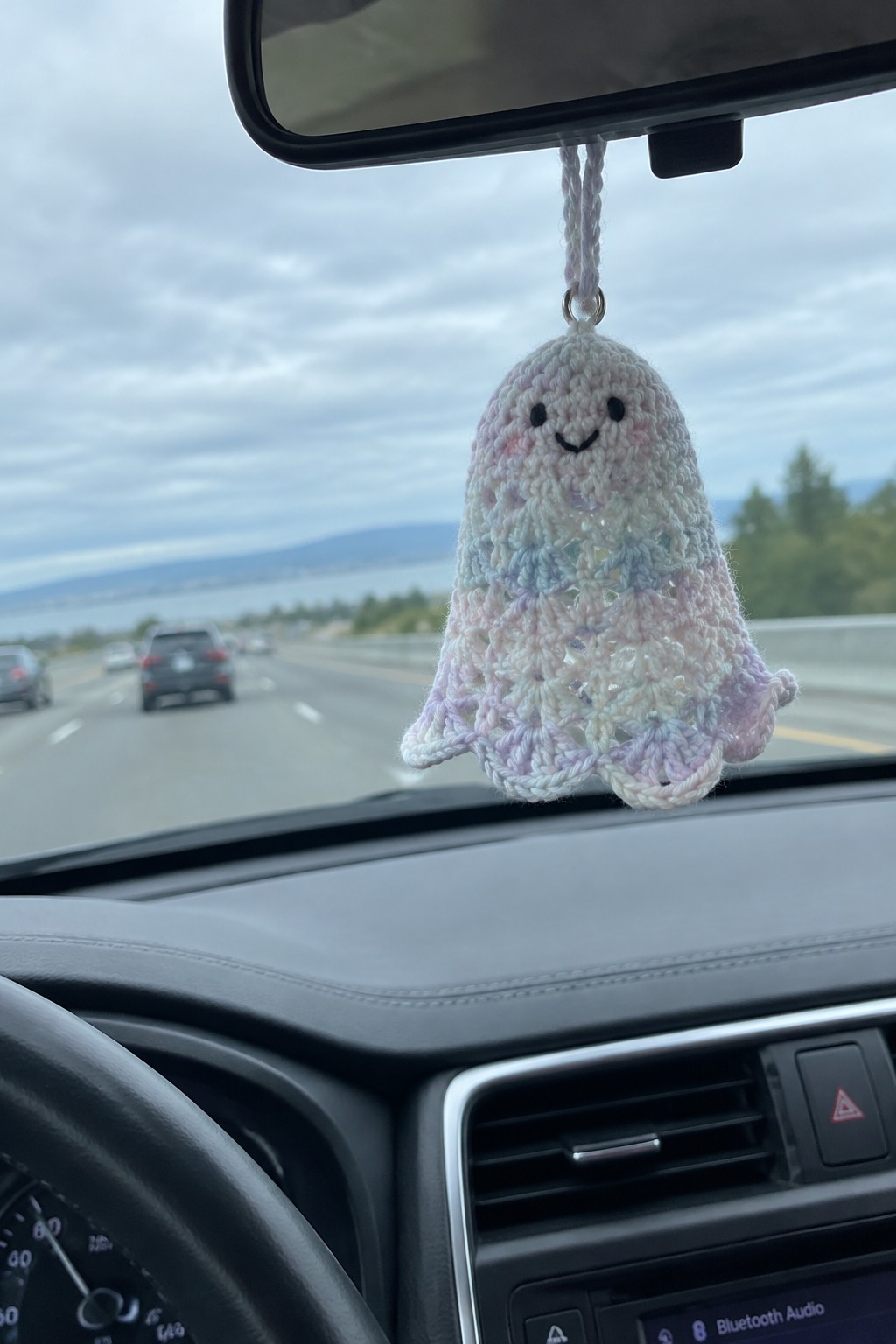 Pastel crocheted ghost ornament dangling from car rearview mirror on highway