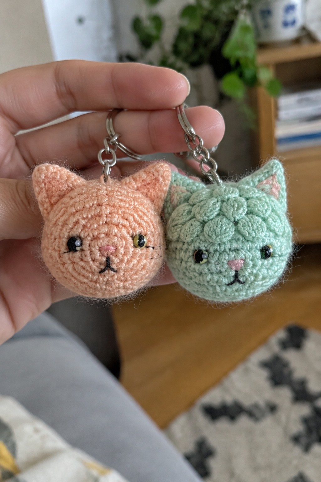 Hand holding peach and mint green crocheted cat keychains with chains.