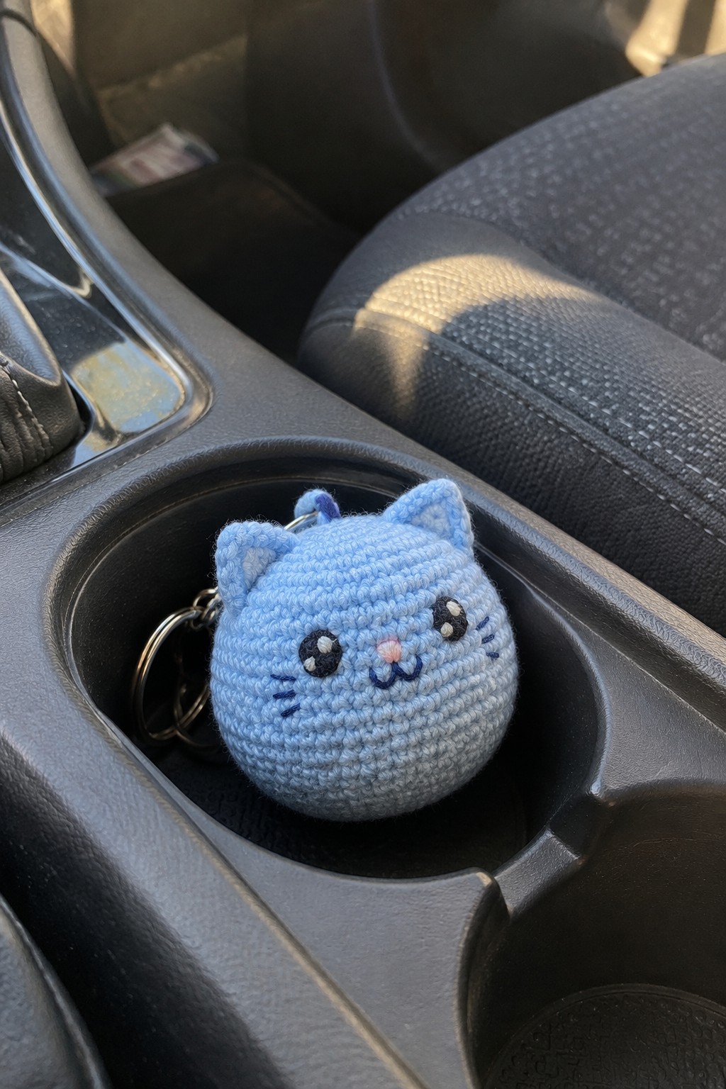Blue crocheted cat keychain in a car's black cup holder