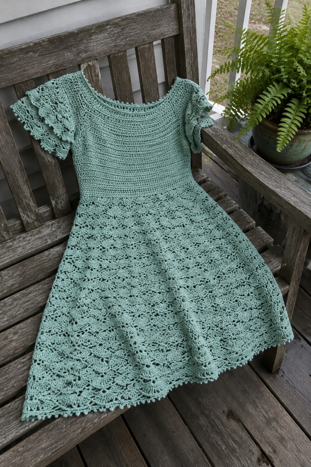 Mint green crocheted lace dress on wooden porch bench beside potted fern