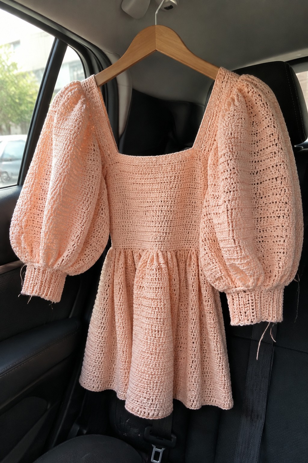 Pink crocheted square-neck top with puff sleeves on wooden hanger in car