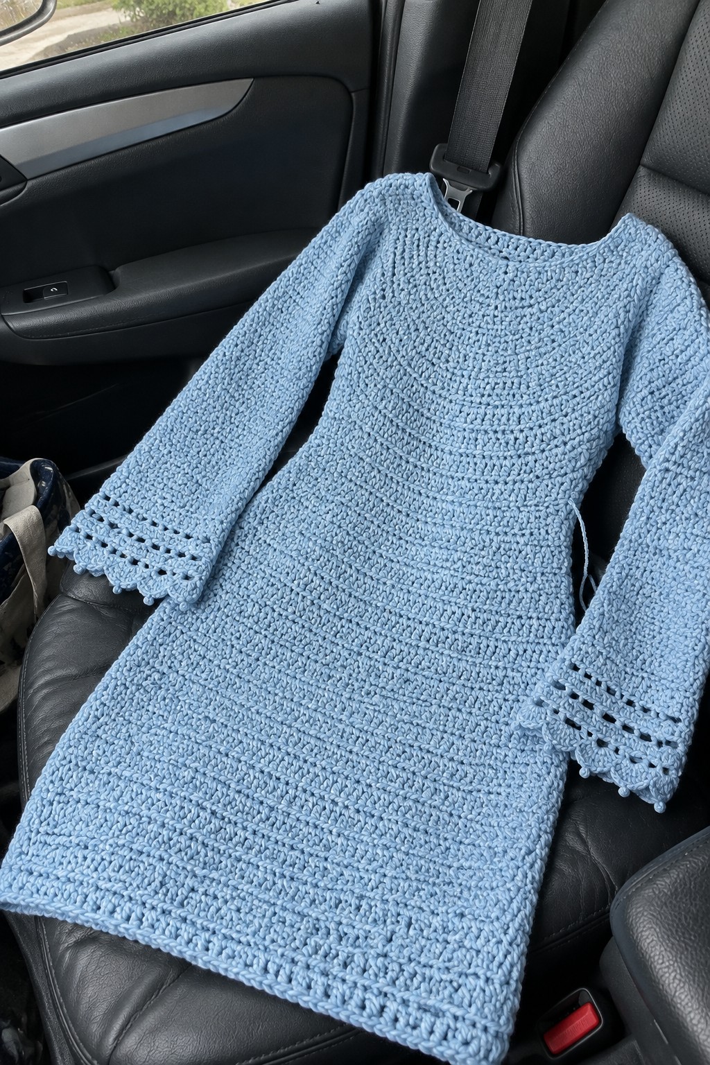 Light blue crocheted dress with long sleeves on black car seat