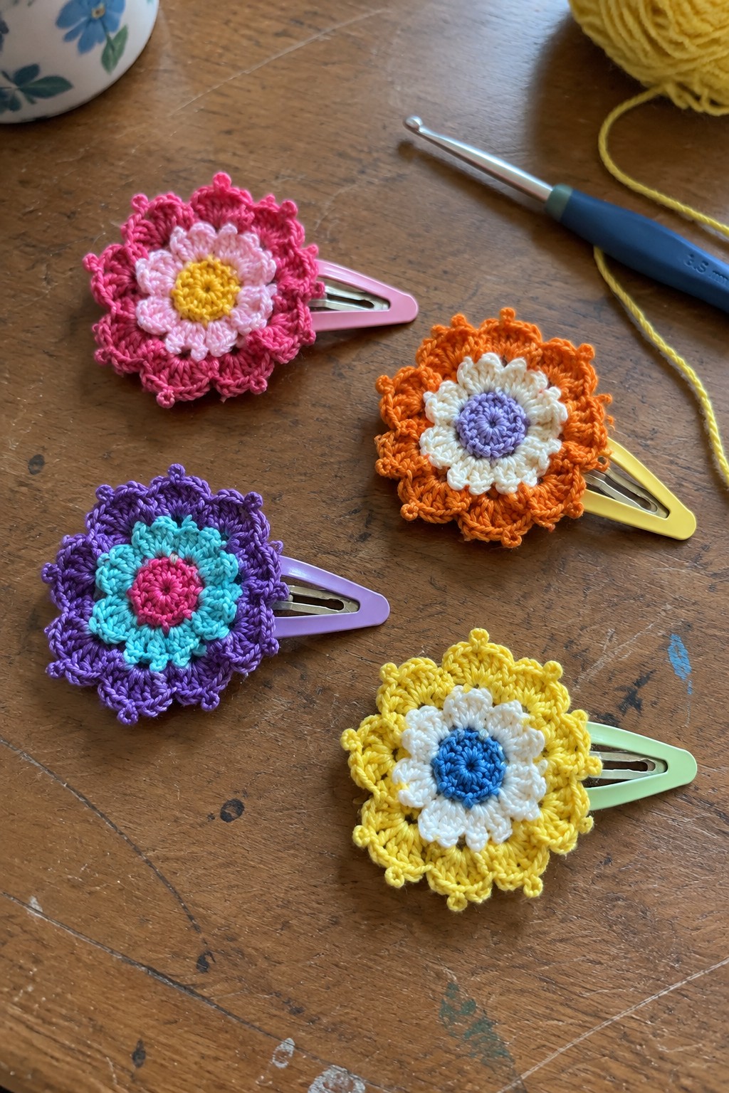 Four colorful crocheted flower hair clips with hook on wooden table