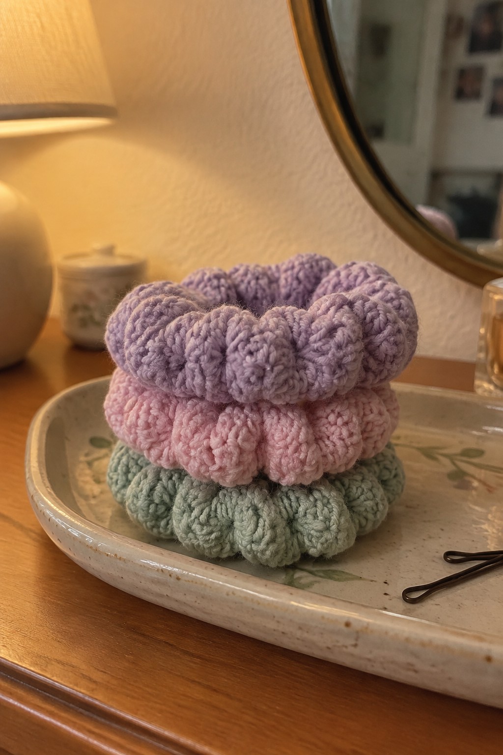 Three pastel crocheted scrunchies stacked on a ceramic tray on wood