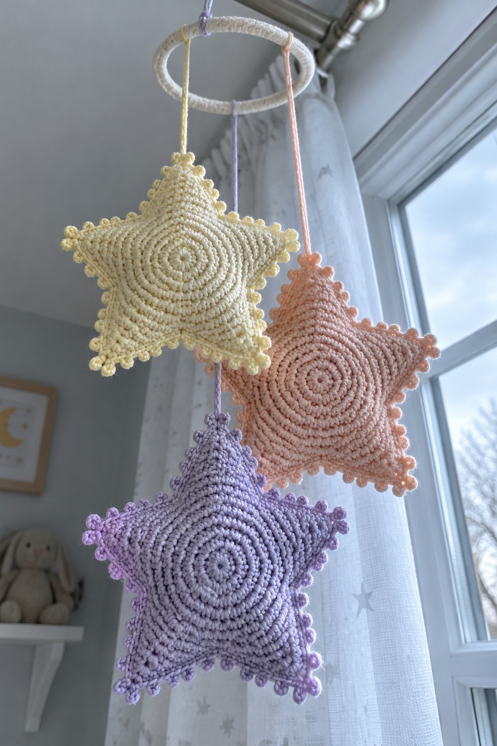Pastel yellow, peach, and purple crocheted stars hanging from a white ring