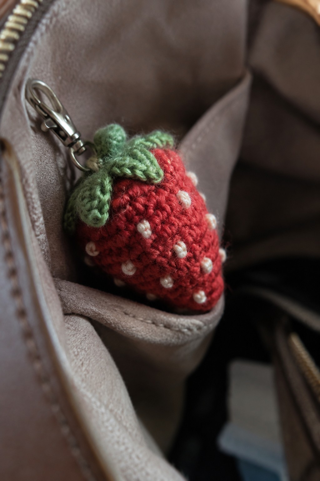Crocheted red strawberry keychain with green leaves on beige bag zipper