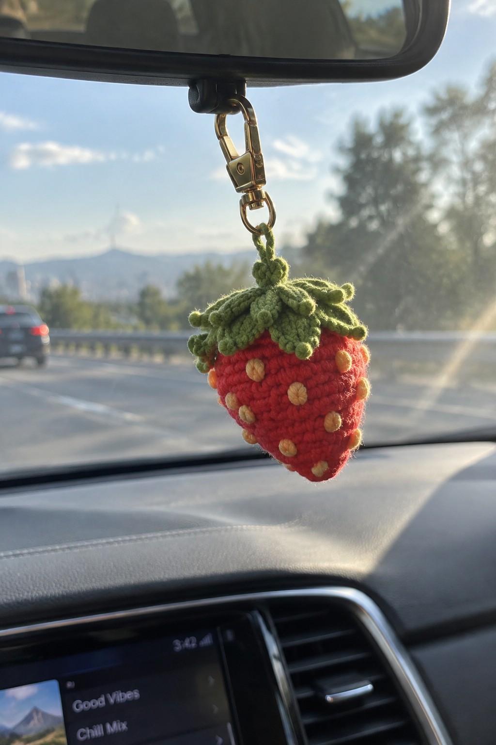 Red crocheted strawberry charm hanging from gold clip on car rearview mirror