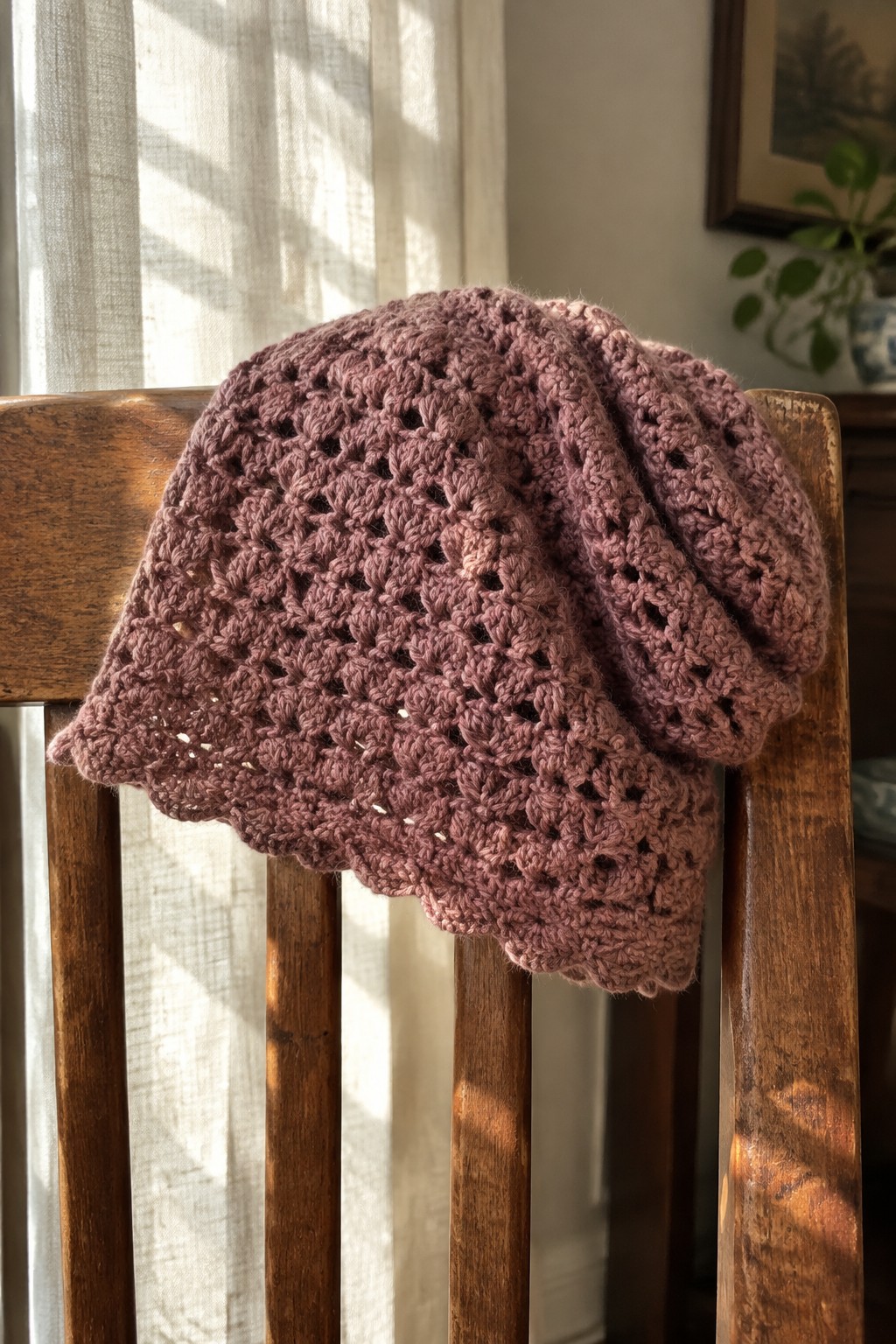 Dusty rose crocheted lace hat draped over wooden chair in sunlight