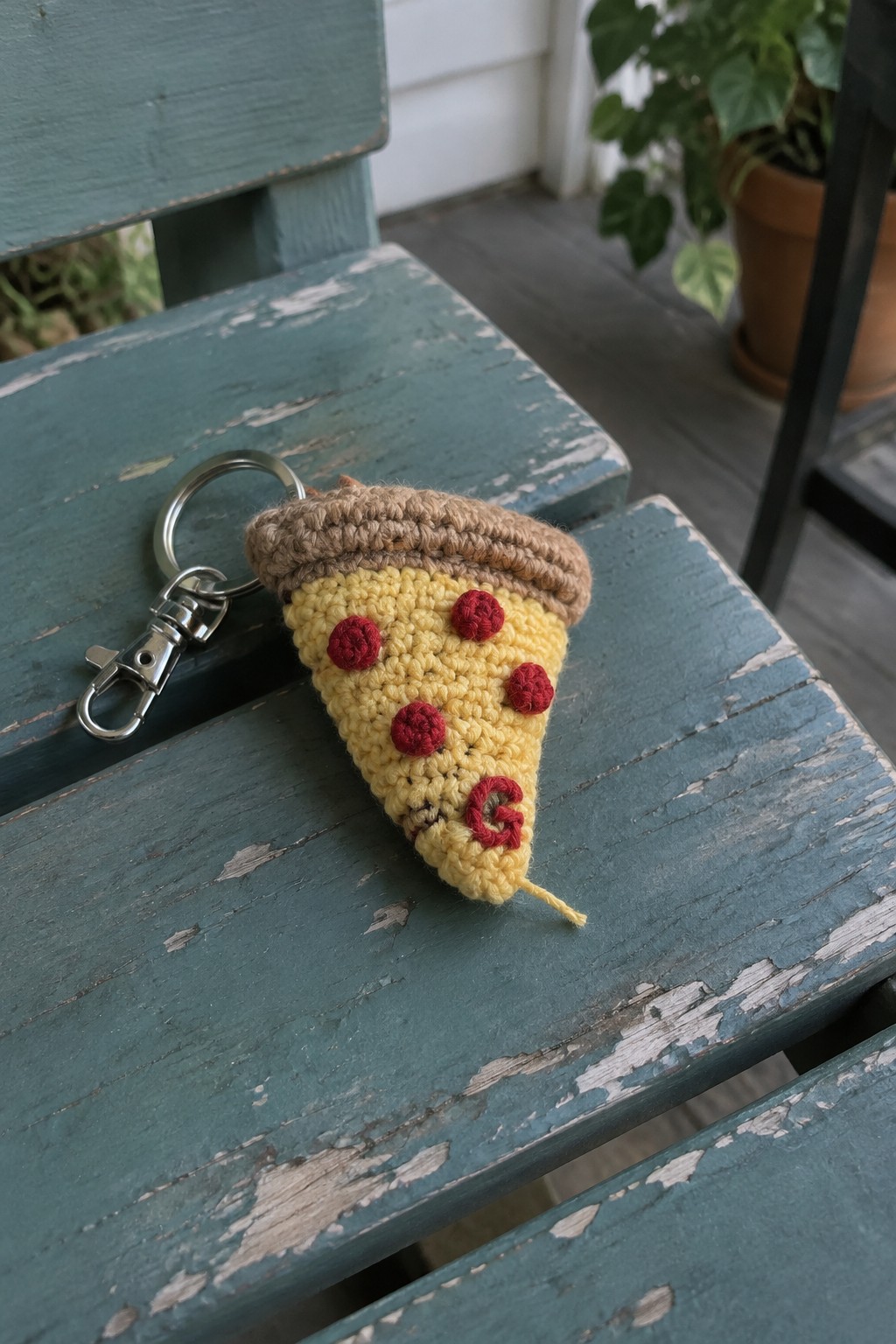 Crocheted yellow pizza slice keychain with red toppings on teal wooden bench