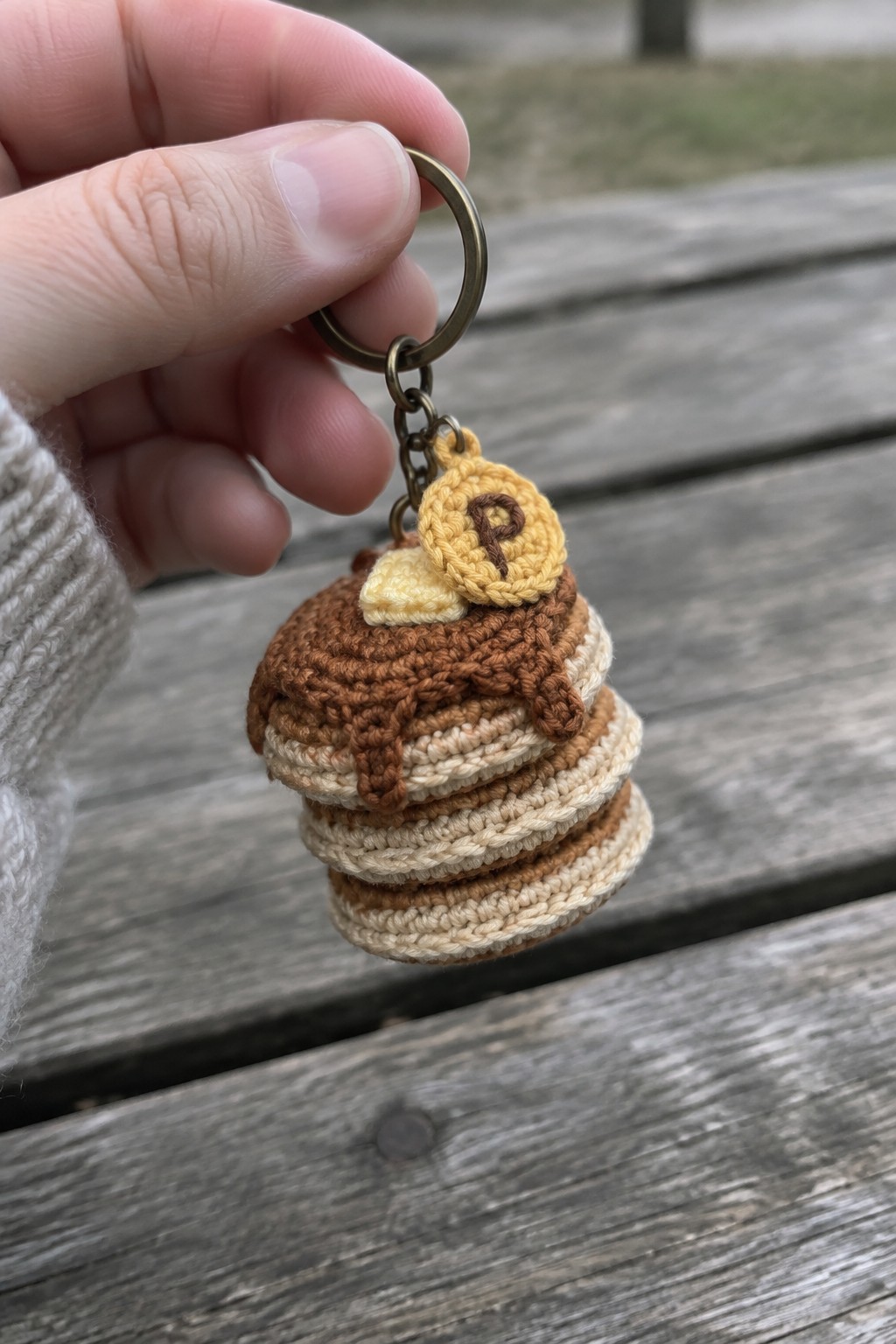 Hand holding crocheted pancake stack keychain with butter and P tag