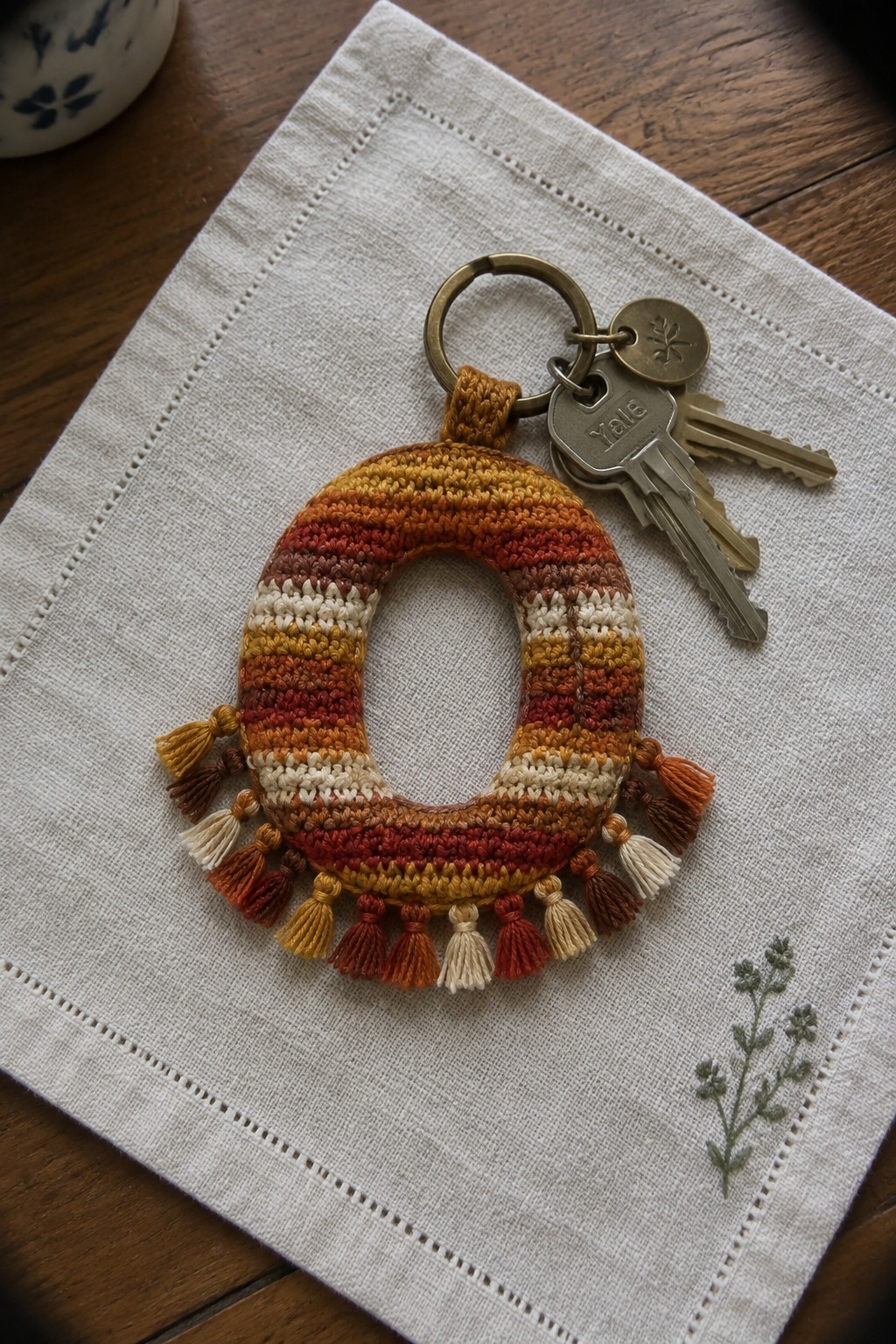 Crocheted keychain in striped autumn colors with tassels on embroidered linen.