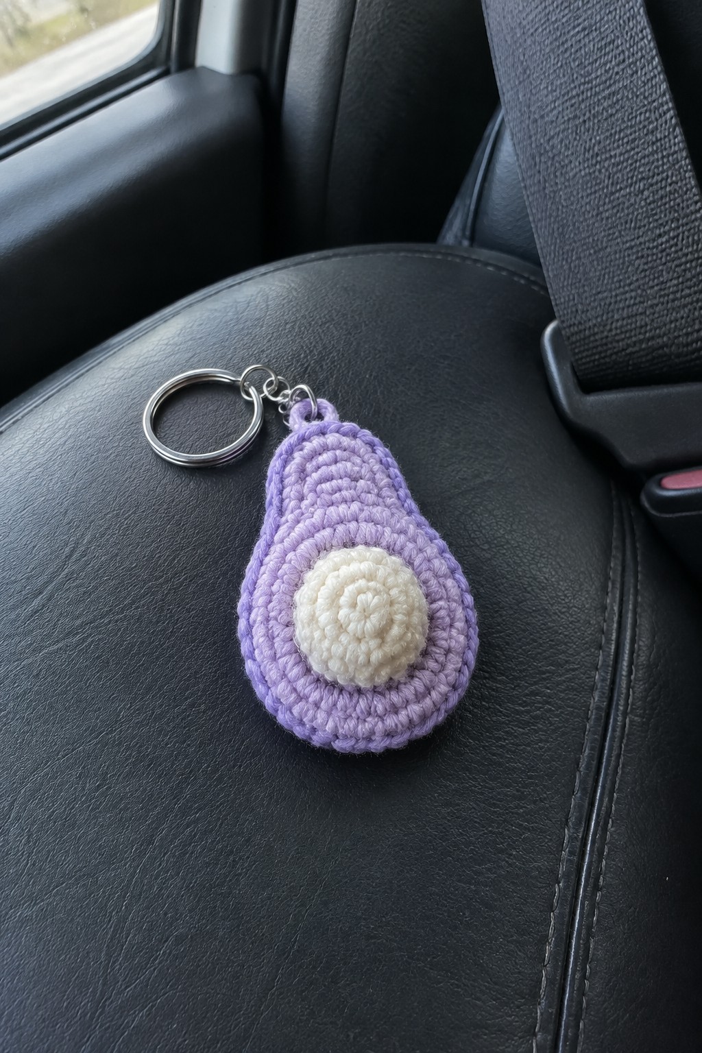 Purple crocheted avocado keychain with white center on black car seat.