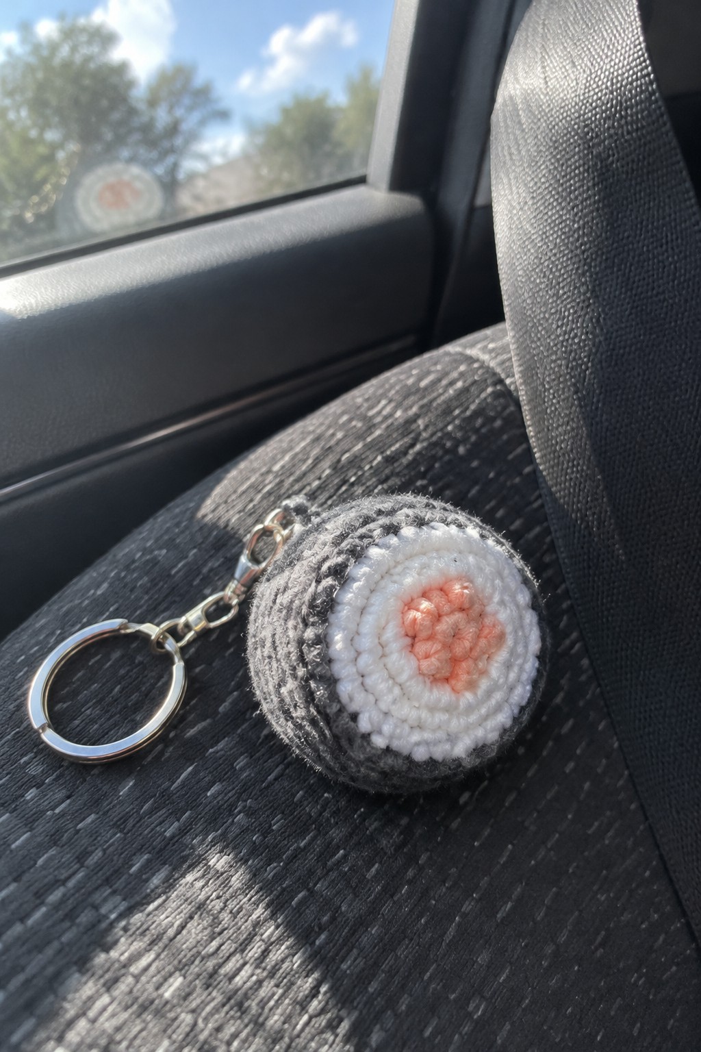 Crocheted sushi keychain with pink center on dark gray car seat