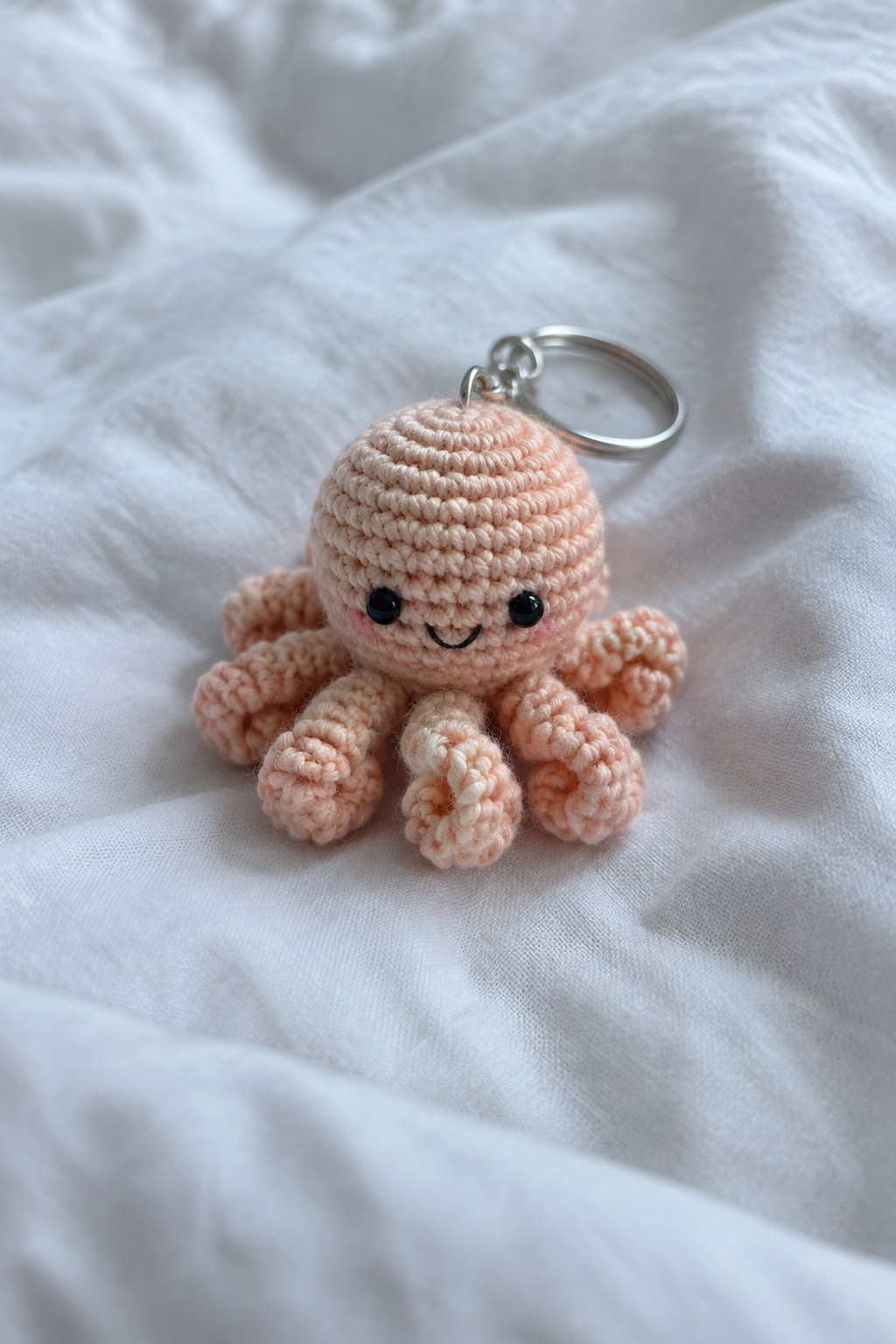 Peach crocheted octopus keychain with smiling face and metal ring on white fabric
