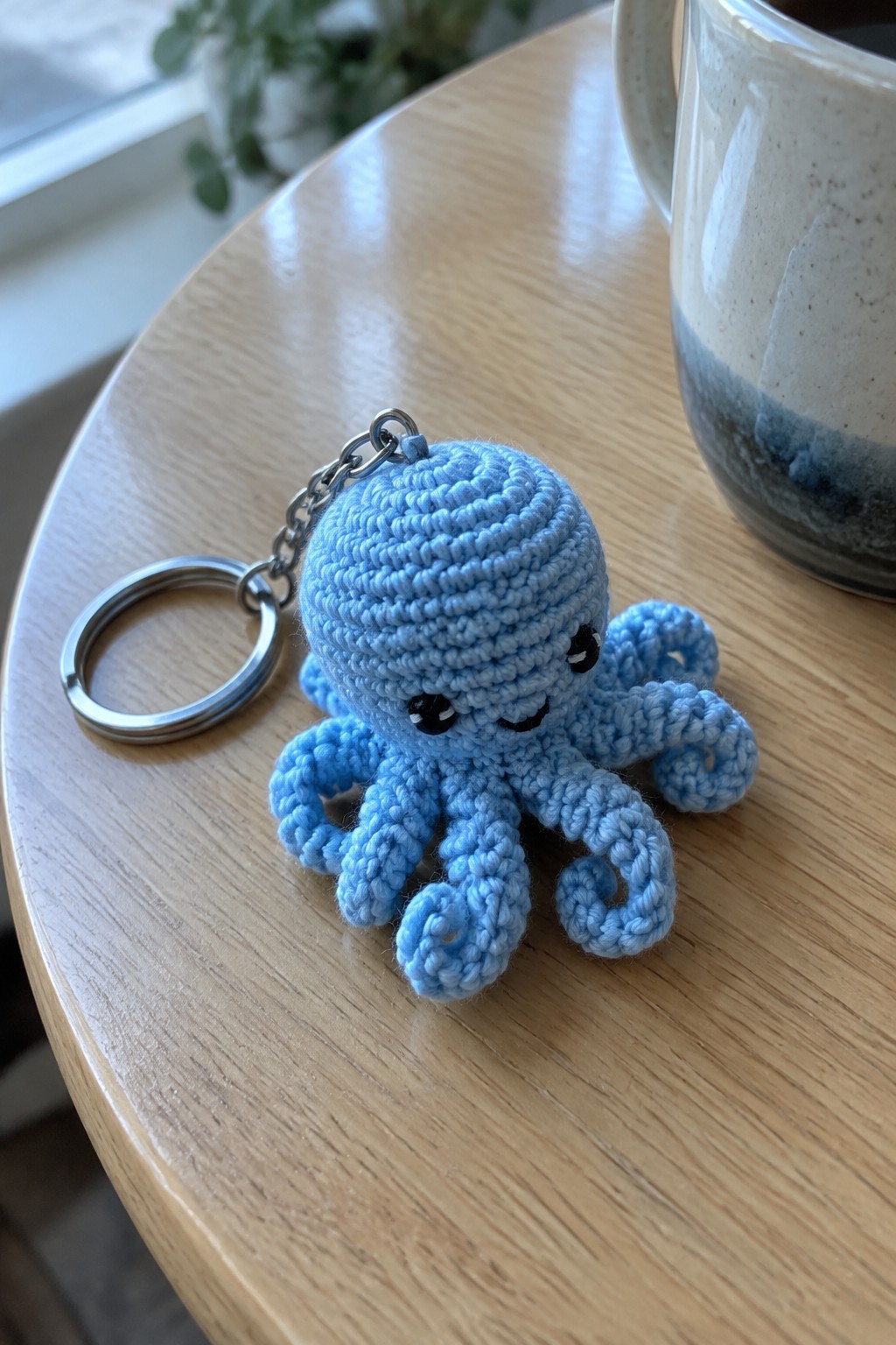 Blue crocheted octopus keychain on wooden table beside speckled ceramic mug
