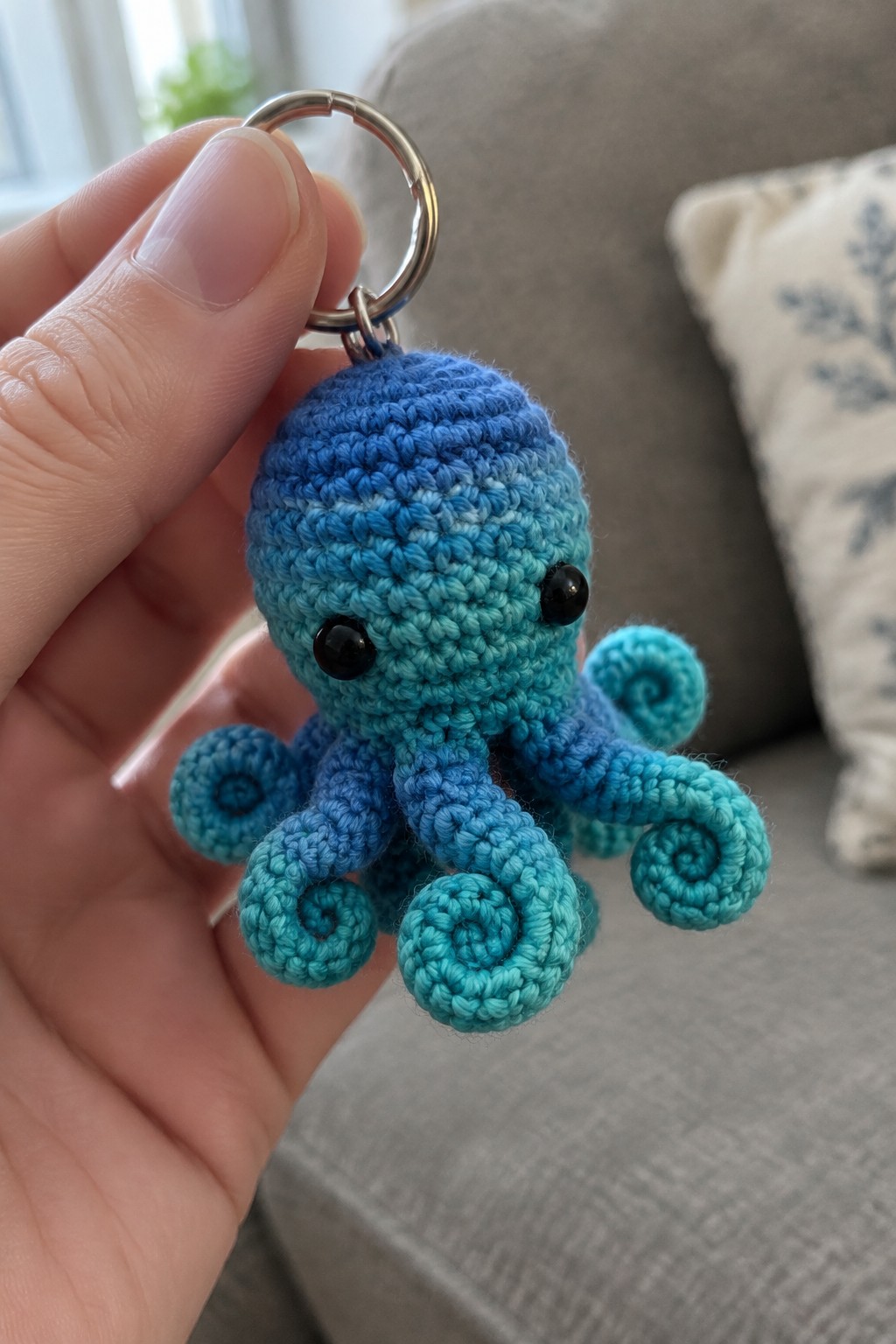 A small crocheted octopus keychain in blue gradient yarn with curled tentacles attached to a metal ring.