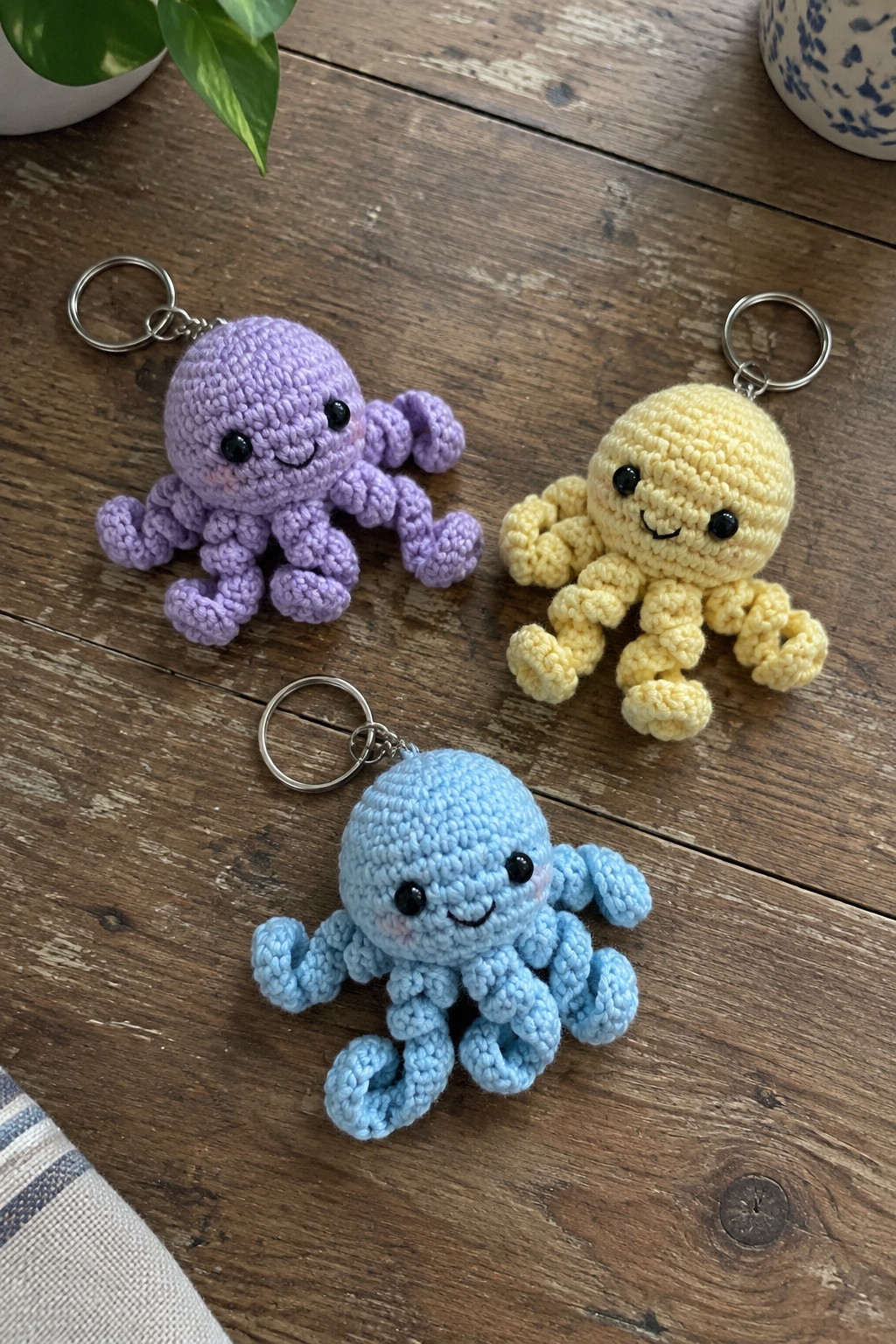 Three colorful crocheted octopus keychains with smiling faces on wooden table