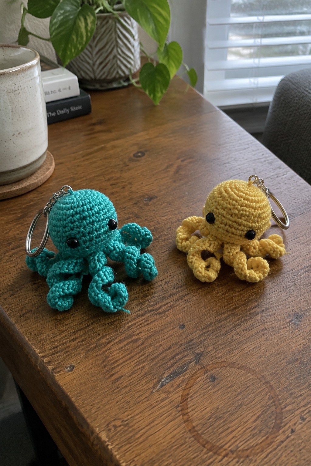Teal and yellow crocheted octopus keychains on wooden table with plant and book