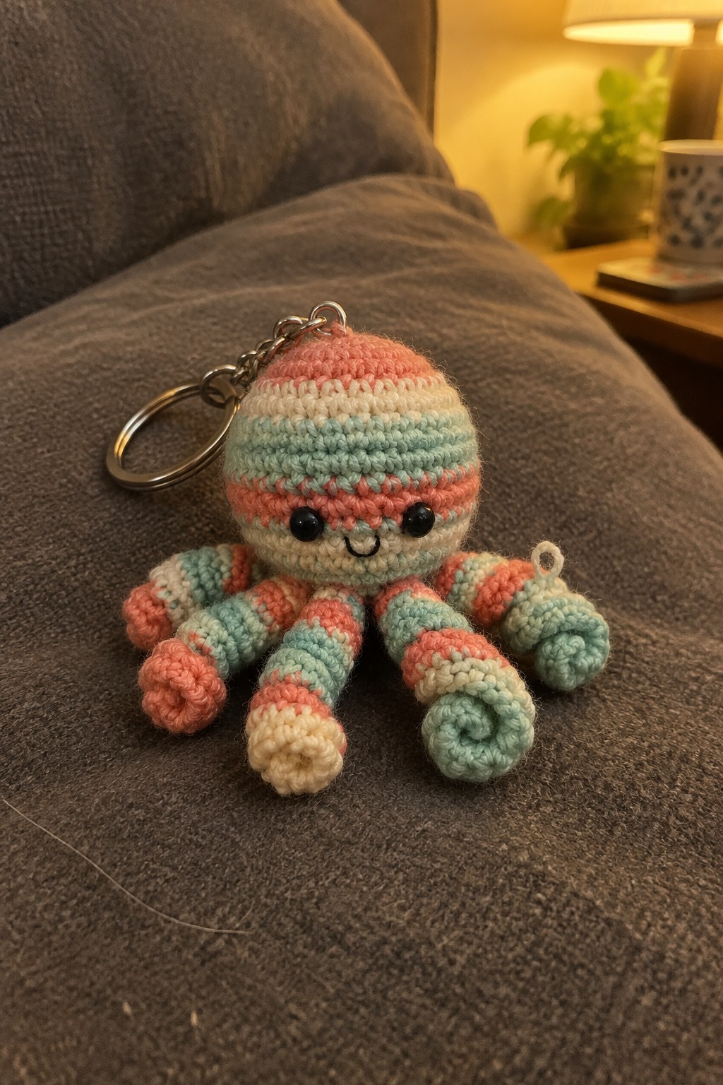 Colorful striped crocheted octopus keychain with black eyes on gray fabric.