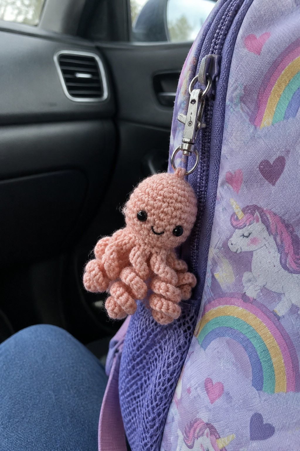 Pink crocheted octopus keychain on purple unicorn backpack inside car