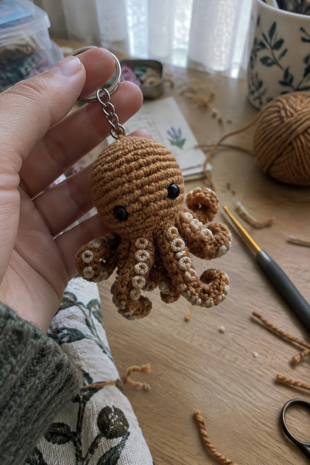 Hand holding brown crocheted octopus keychain with beige suckers on wooden table.