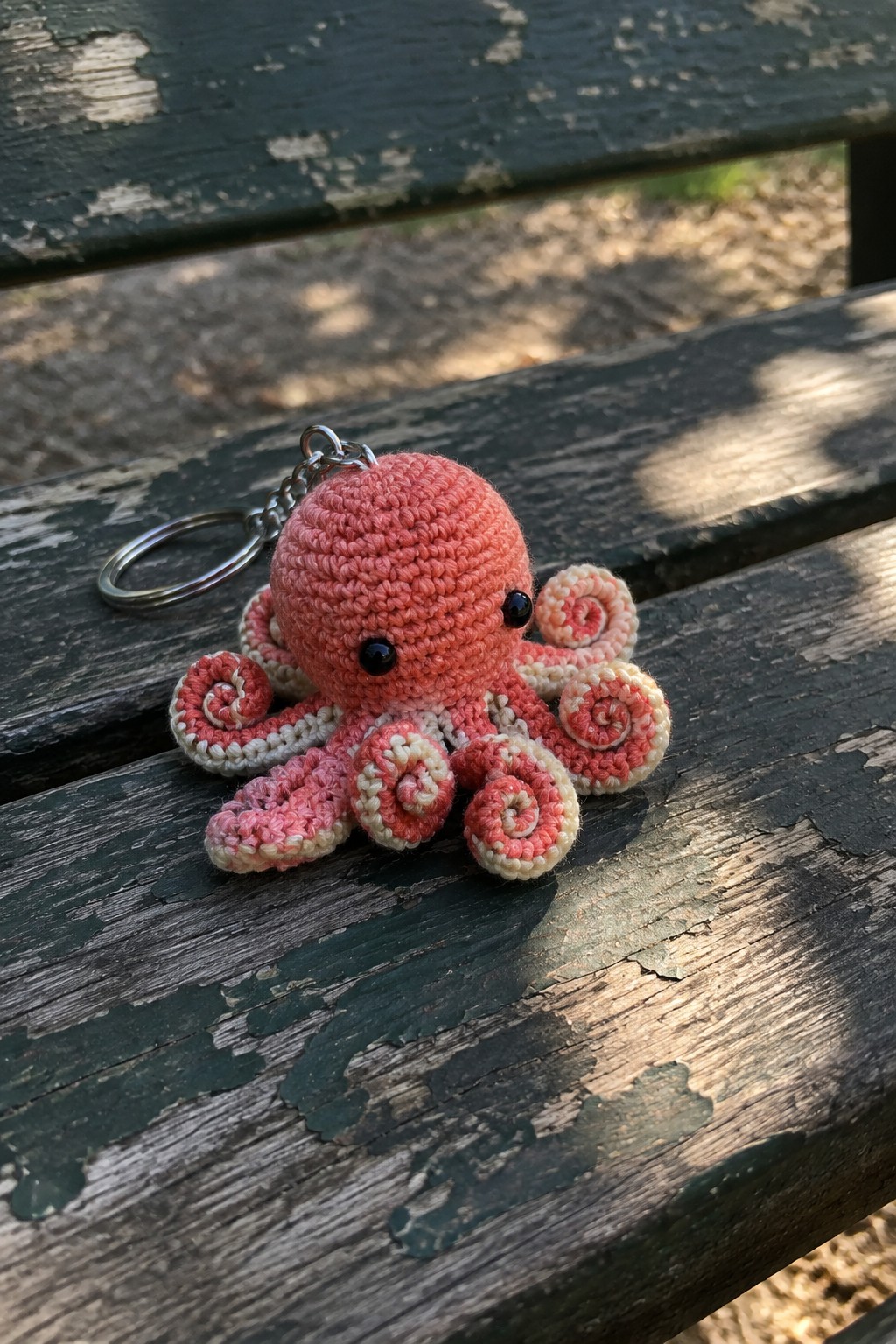 Pink crocheted octopus keychain with spiral tentacles on weathered wood.
