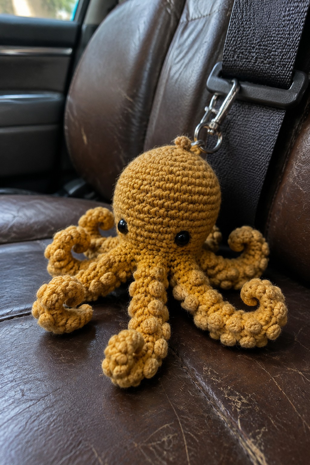Yellow crocheted octopus toy on brown leather car seat beside seatbelt
