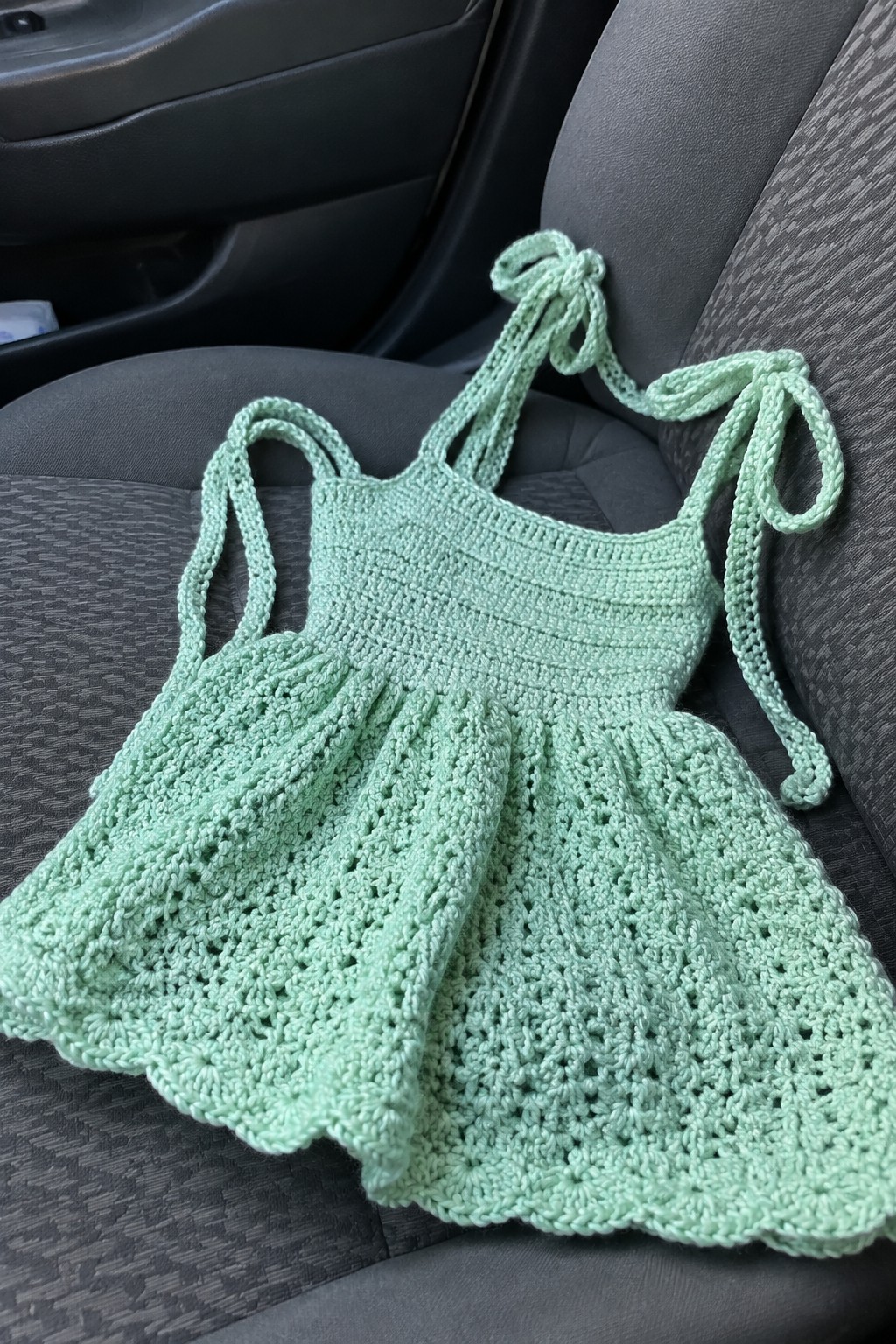 Light mint green crocheted dress with tie straps on a gray car seat.