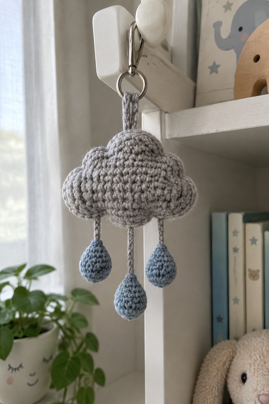 Gray crocheted cloud with blue raindrops hanging from white hook by metal clip